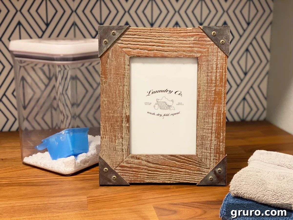 A tastefully arranged wooden picture frame holding a 'Laundry Co.' printable sits beside a clear container of laundry detergent, adding a touch of rustic charm to the laundry space.