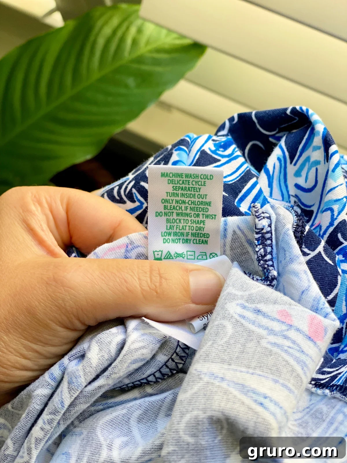 Your Printable Laundry Cheat Sheet 6 A hand holding a clothing tag, with various laundry symbols visible, emphasizing the importance of reading care labels.