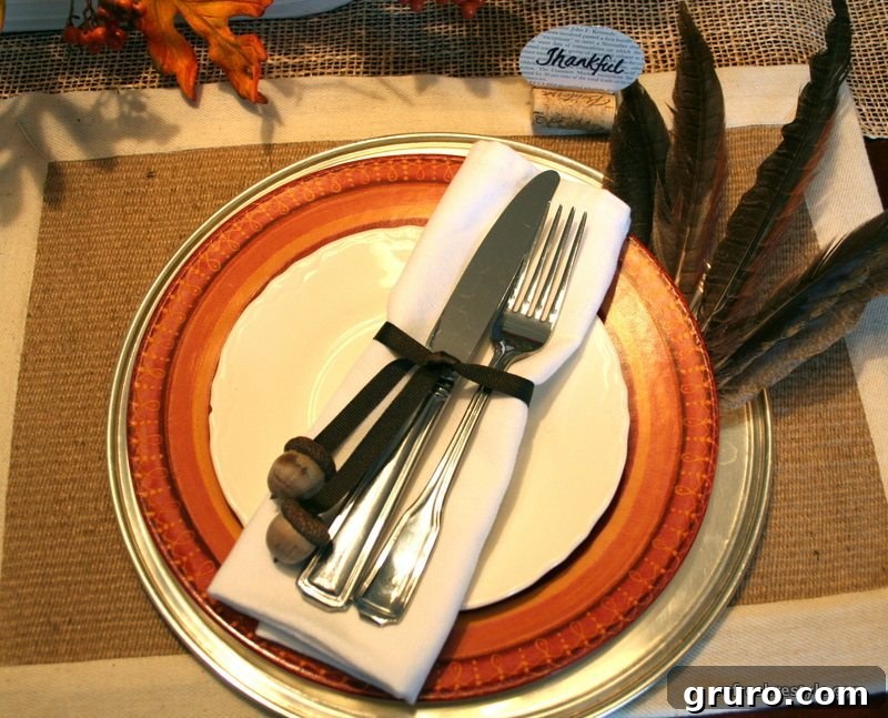 Detailed view of a holiday place setting with wine cork place card holders, acorn-tied silverware, and feathers on a charger plate.