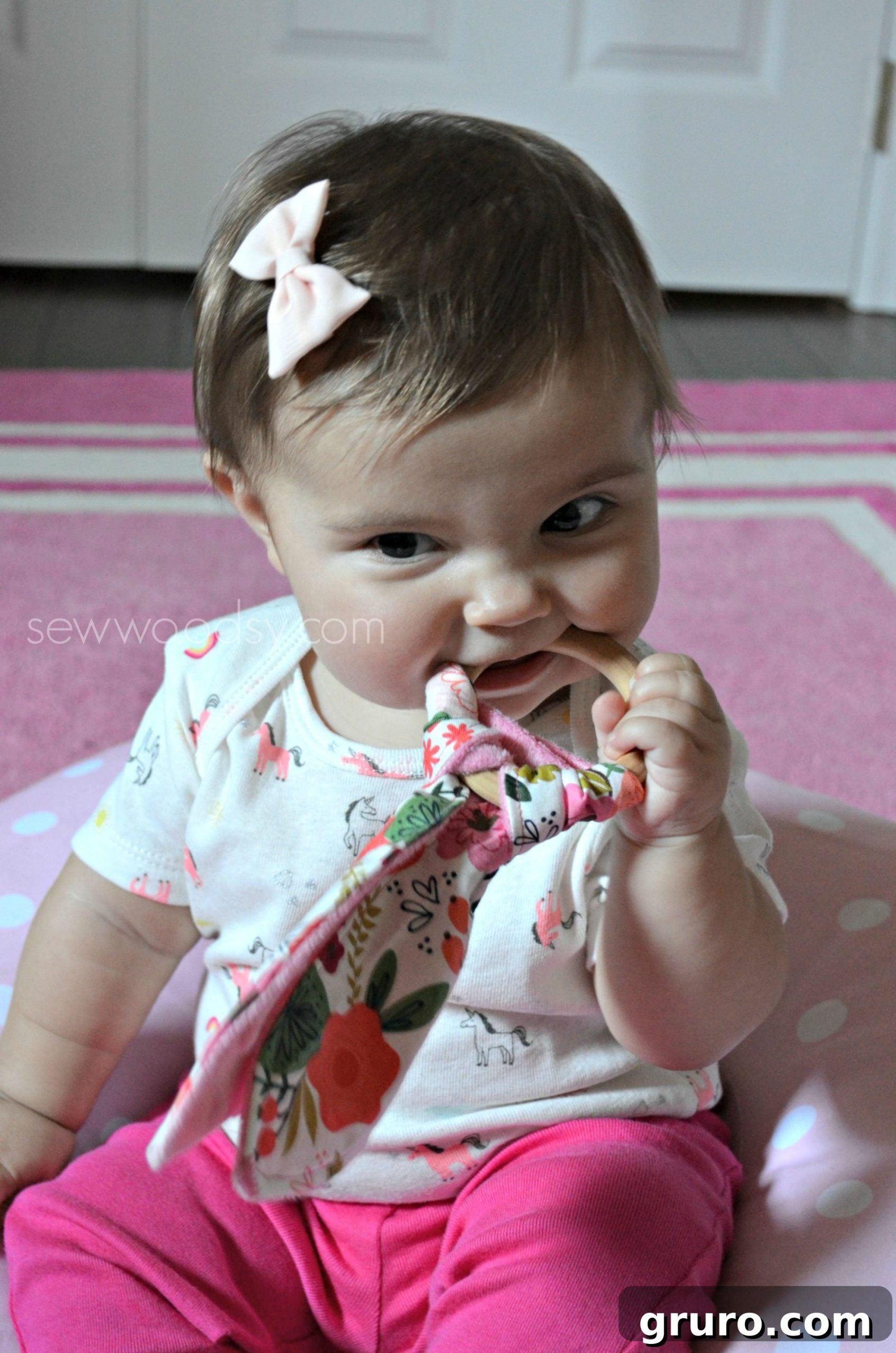 Baby girl chewing on a wooden teething ring.