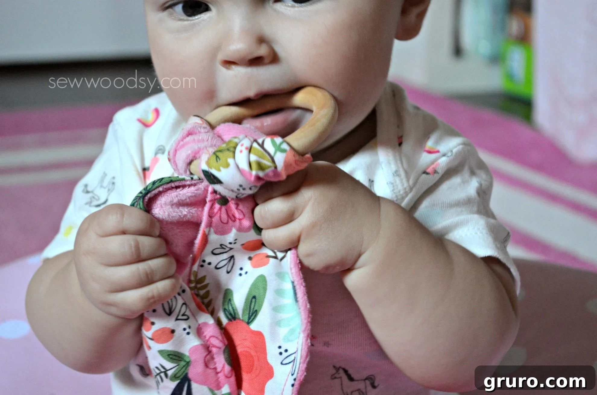 Close up of a baby girl holding a teething ring in mouth.
