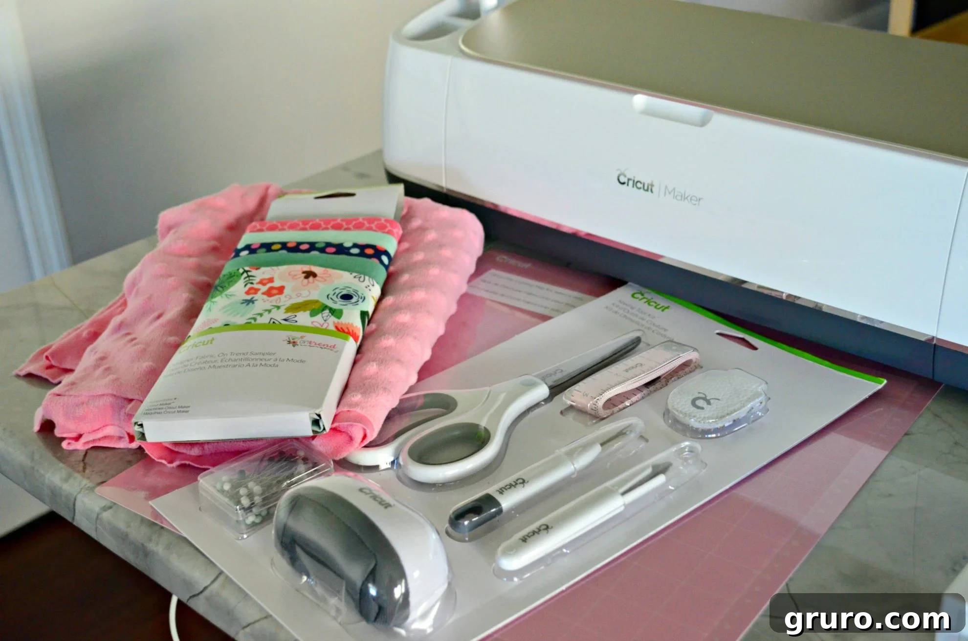 supplies on countertop: fabric, Cricut Maker, pink mat, and sewing supplies.