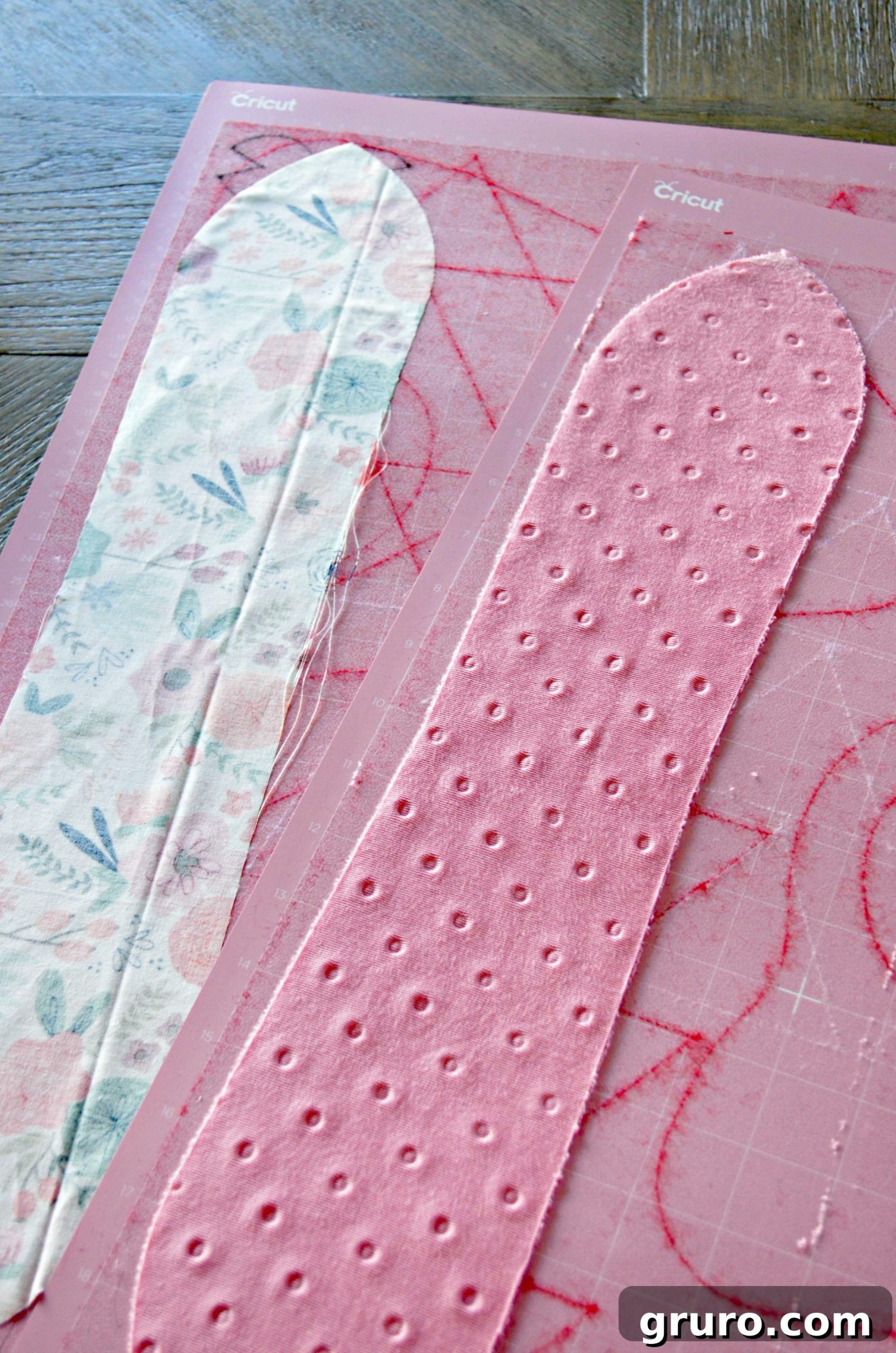 Two pink Cricut cutting mats with two pieces of cut fabric on them.
