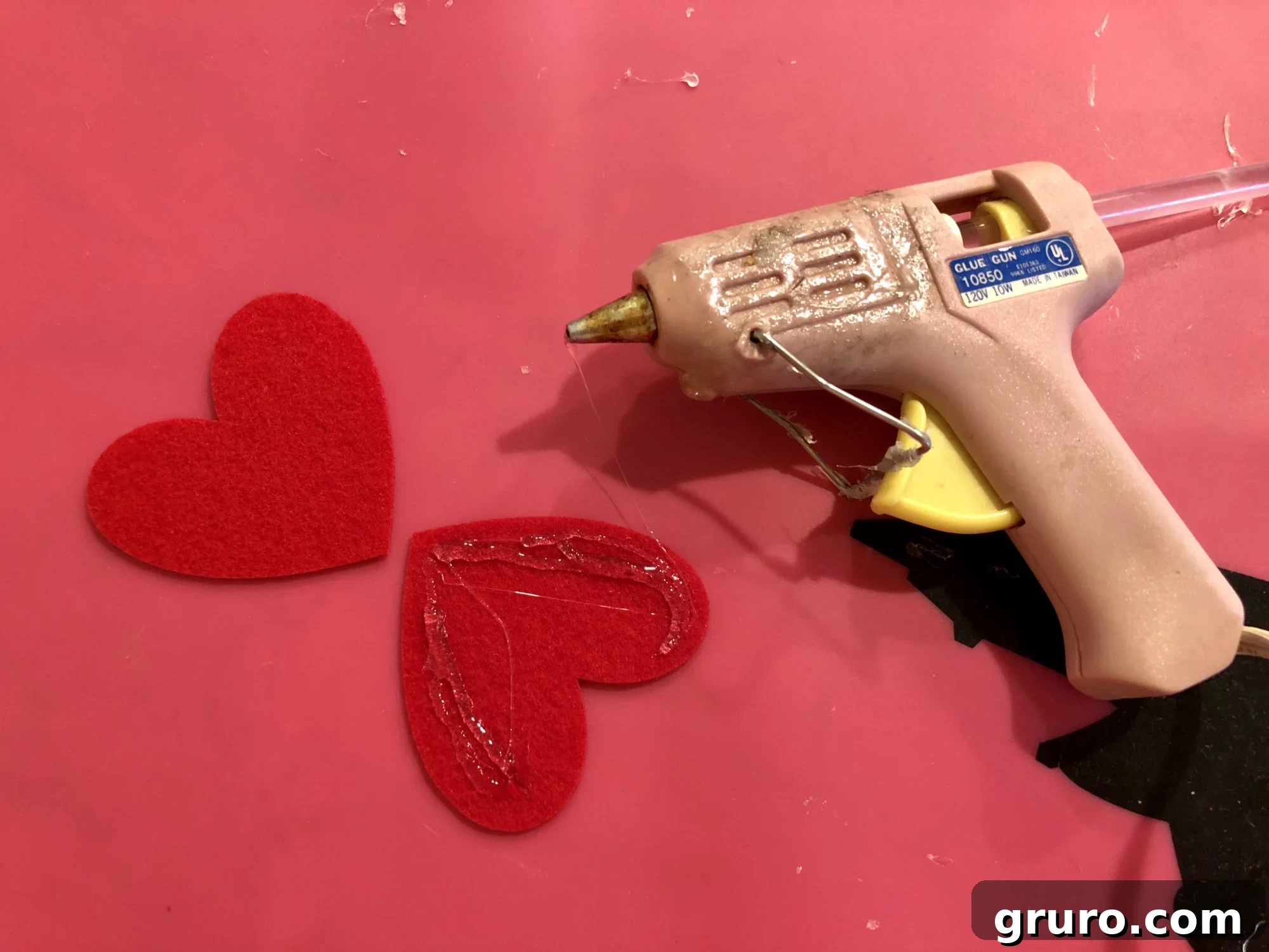 Applying hot glue to three-quarters of a felt heart for assembly