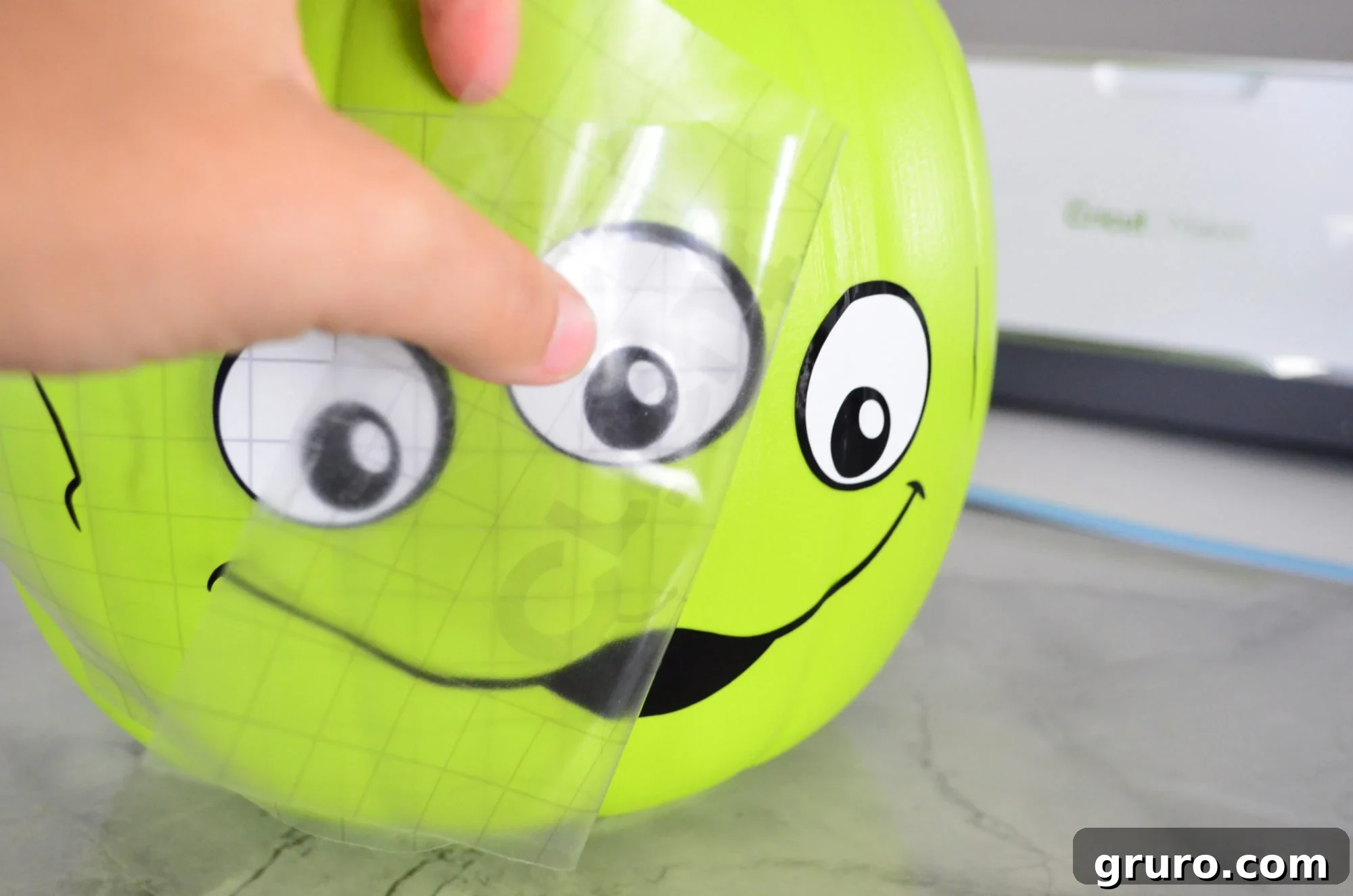 Applying transfer tape with the Alien vinyl design onto the green trick or treat bucket