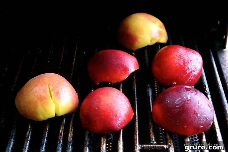 Halved peaches and nectarines cooking on a grill, exhibiting attractive char marks on their cut surfaces.