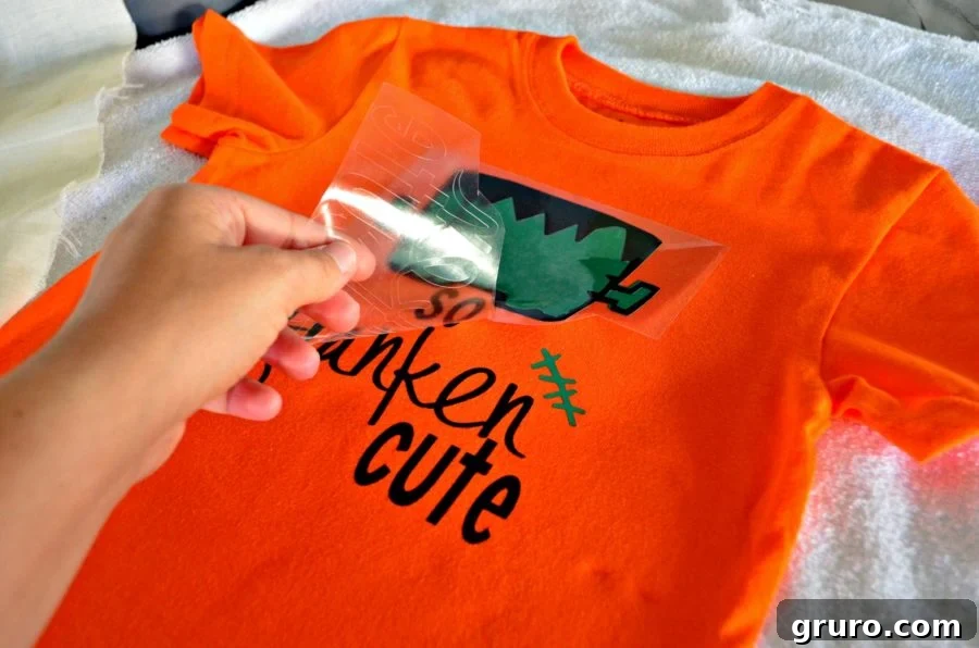 Warm peeling the plastic carrier sheet from the completed 'So Franken Cute' Iron-On Vinyl design on the Halloween shirt