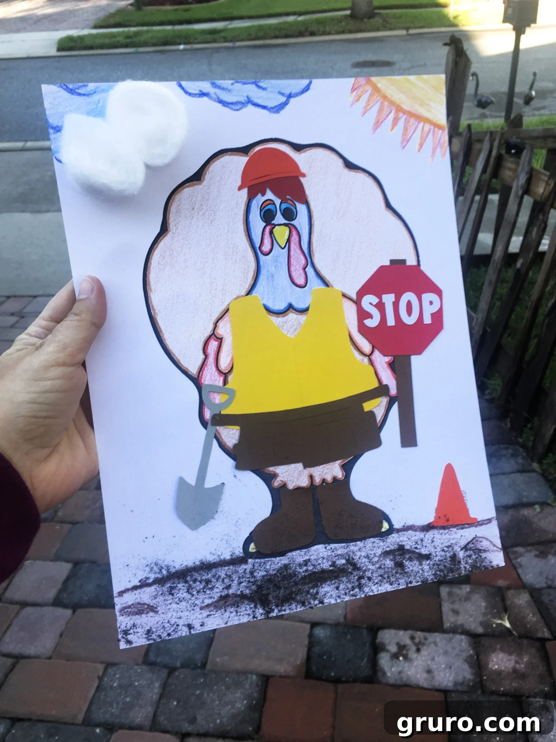 Female hand holding a paper of a Turkey In Disguise as a Construction Worker with a vest, tool belt, and stop sign with dirt on the bottom.