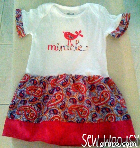 White onesie with the word "miracle" on the shirt with a charming paisley skirt and coordinating arm cuffs.