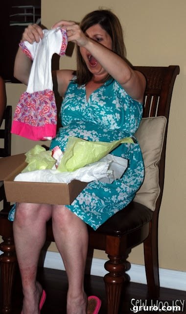 Pregnant women in shock by baby dress with an open box on lap, demonstrating the joy of receiving a handmade gift.