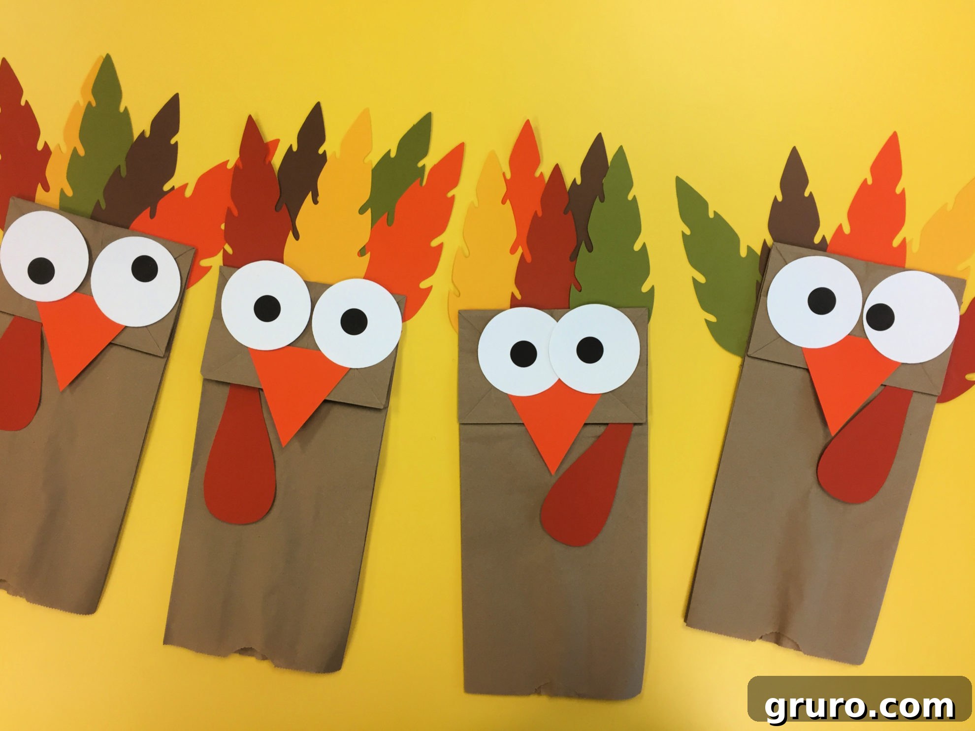 DIY Turkey Paper Bag Puppets 12 Four adorable Turkey Paper Bag Puppets posing together on a cheerful yellow table, showcasing their individuality and festive charm, ready for the holidays.