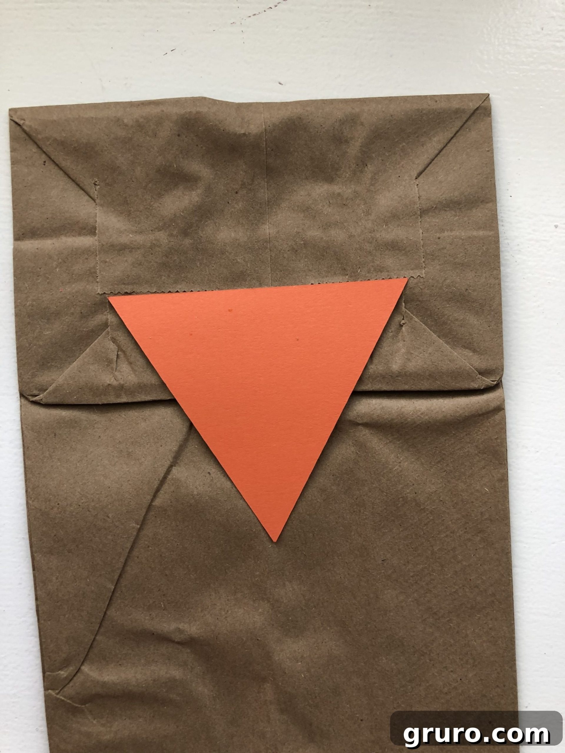 DIY Turkey Paper Bag Puppets 5 A top-down view of a brown paper bag, with an orange triangle meticulously glued onto the front flap, forming the turkey's beak, perfectly aligned.