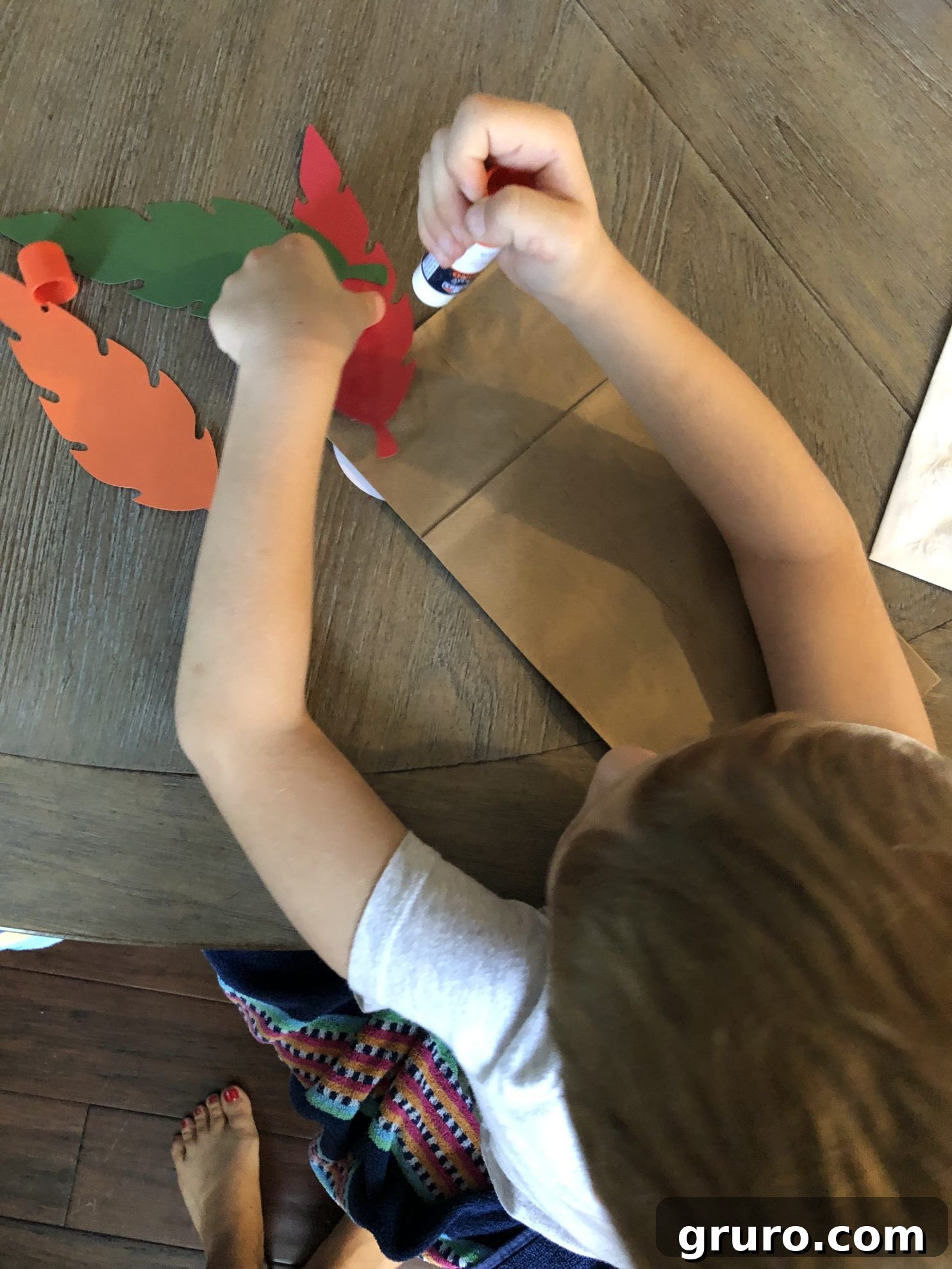 DIY Turkey Paper Bag Puppets 9 A charming image of a little boy intently gluing colorful paper feathers onto the back of a brown paper bag, engrossed in his craft and adding character to his turkey.