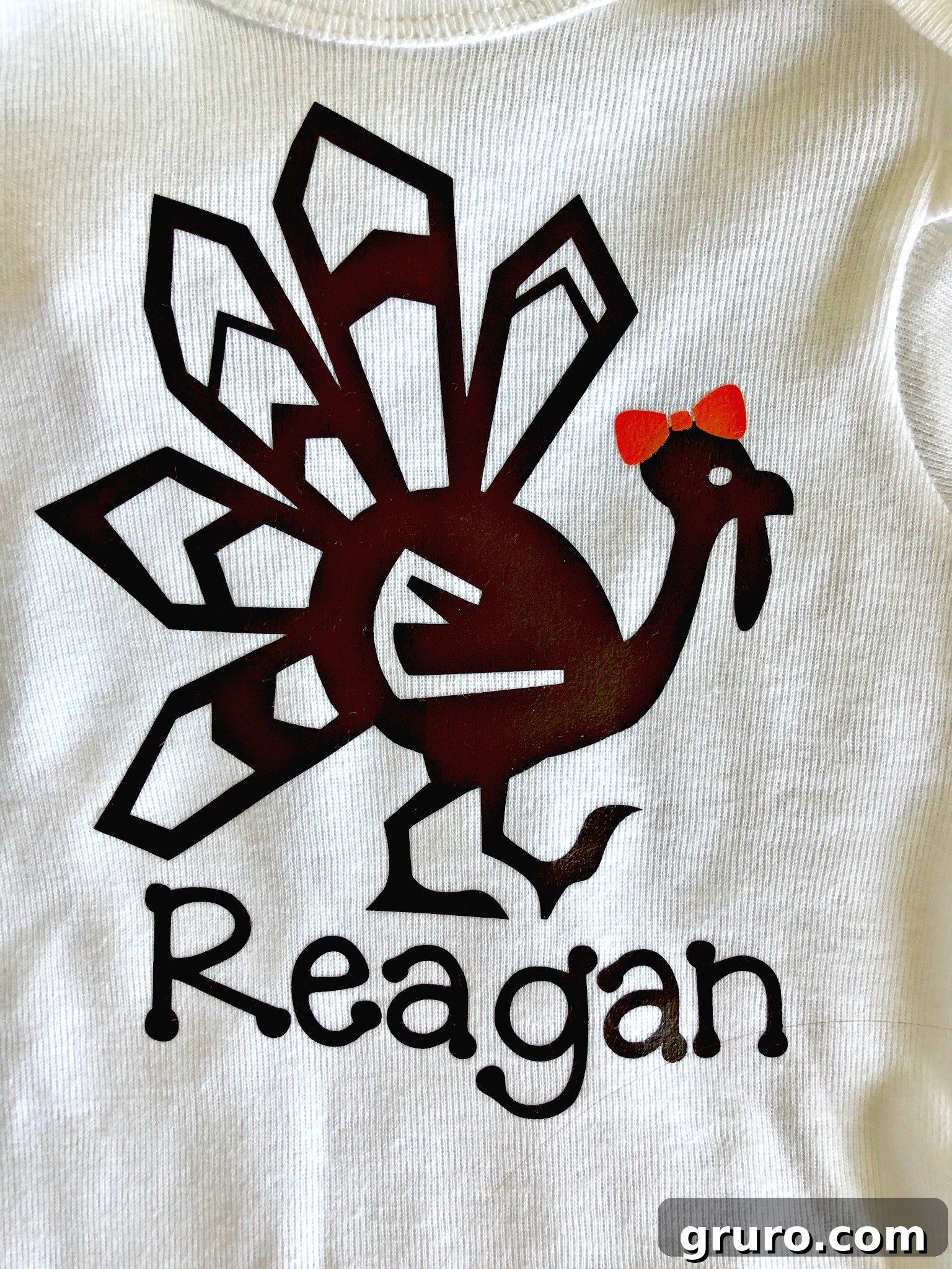 Close-up of a personalized Thanksgiving turkey shirt for a girl, featuring a brown turkey, an orange bow, and the name 'Reagan' in a whimsical font.