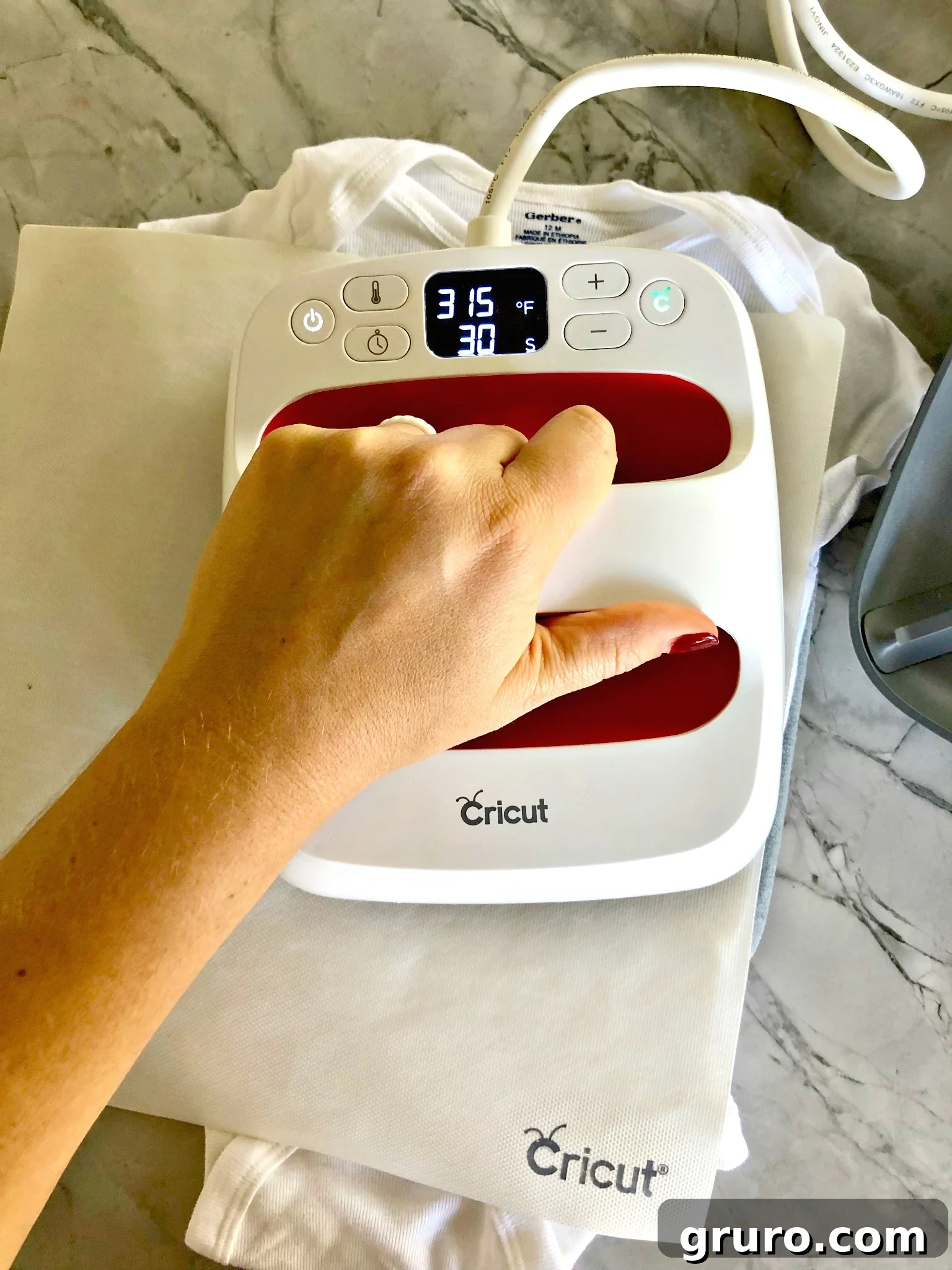 Female hand using a Cricut EasyPress Mini on a baby onesie with a turkey design, ensuring firm heat application.