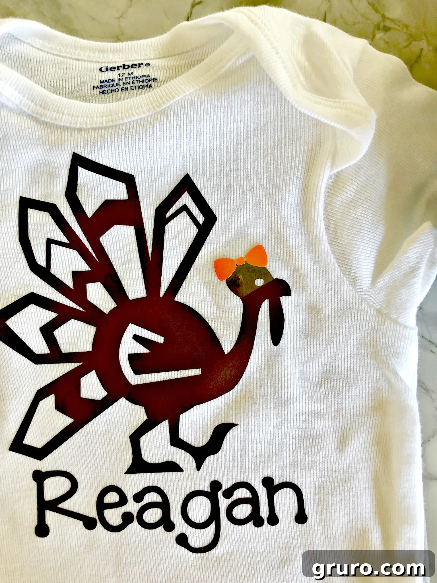 A white onesie with a brown turkey and personalized name, with an orange bow being carefully positioned for the next pressing step.