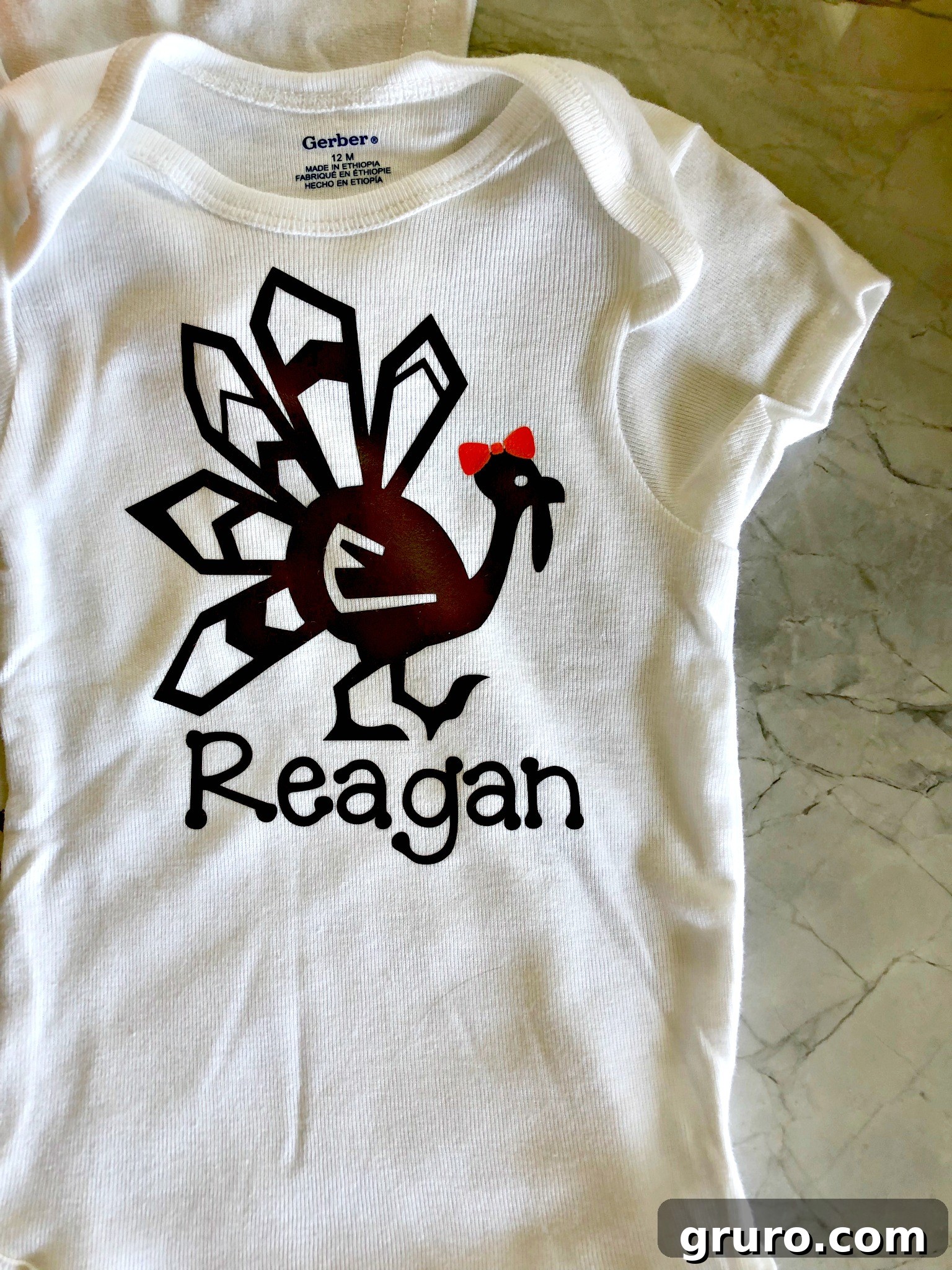 Top view of a completed white onesie featuring a brown turkey design with an orange bow and a child's name, ready for Thanksgiving.