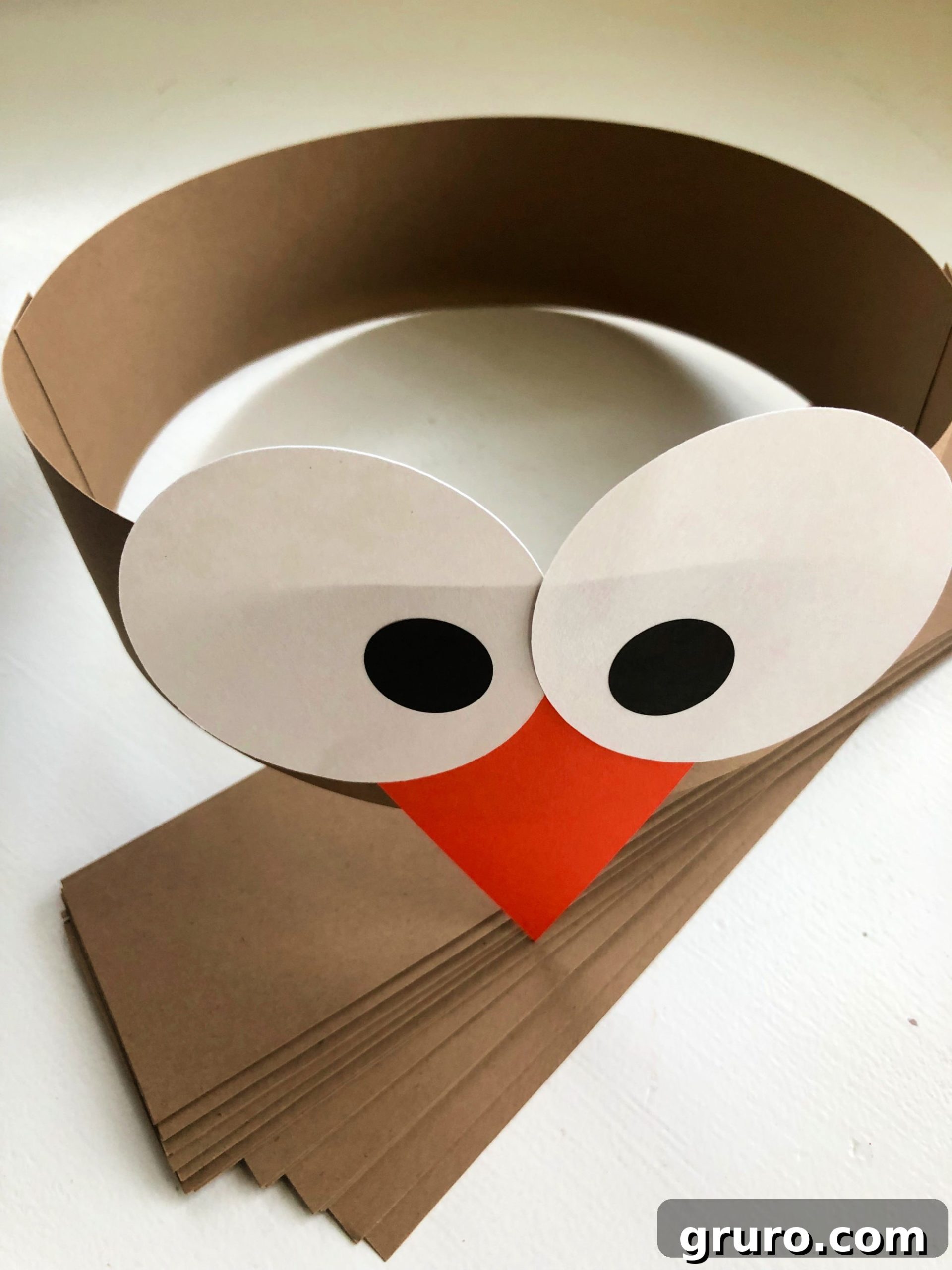 Brown paper headband with white circle and black pupil stickers with an orange triangle beak.