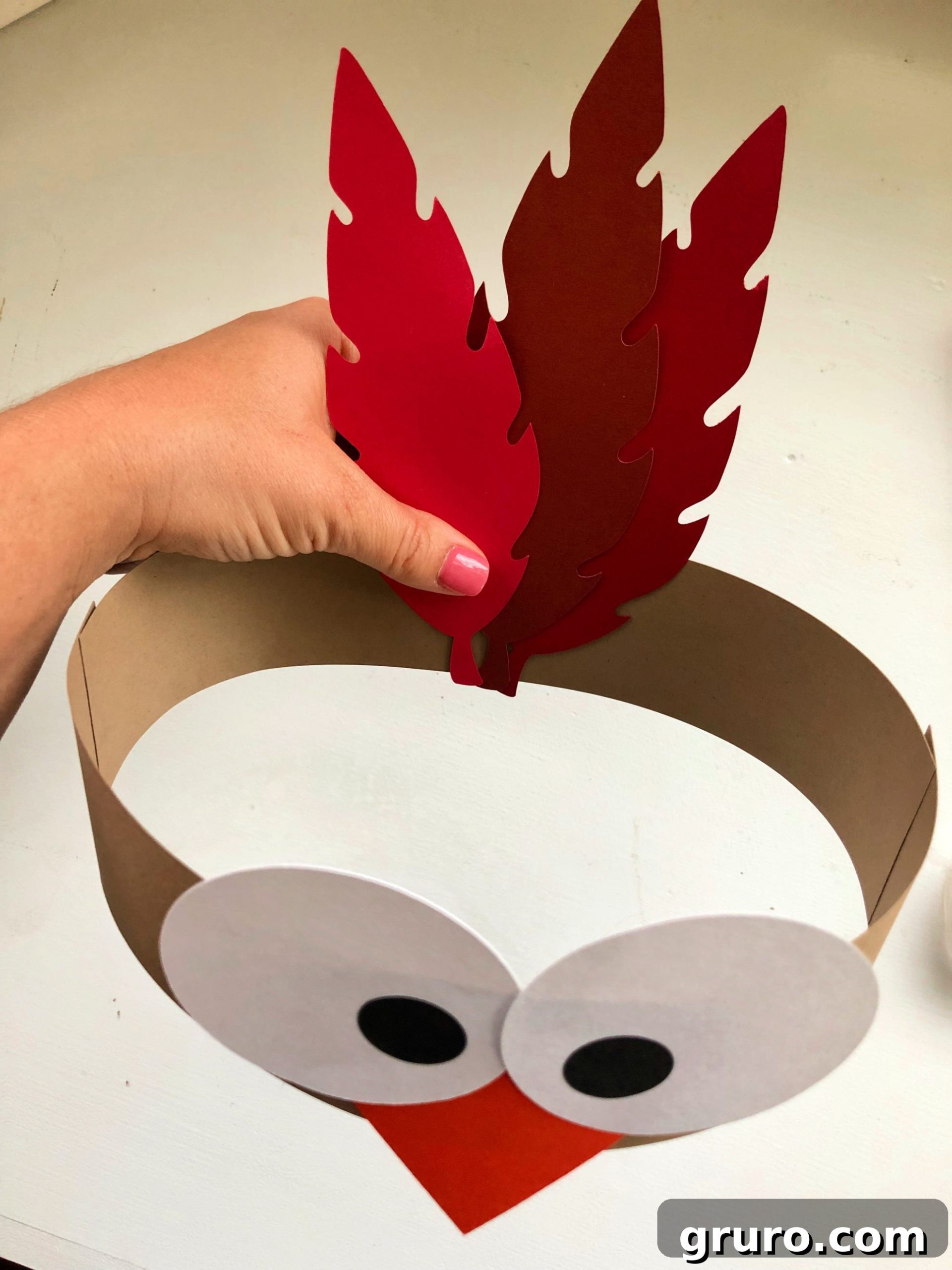 Female hand pressing paper feathers to the back of a brown paper headband.