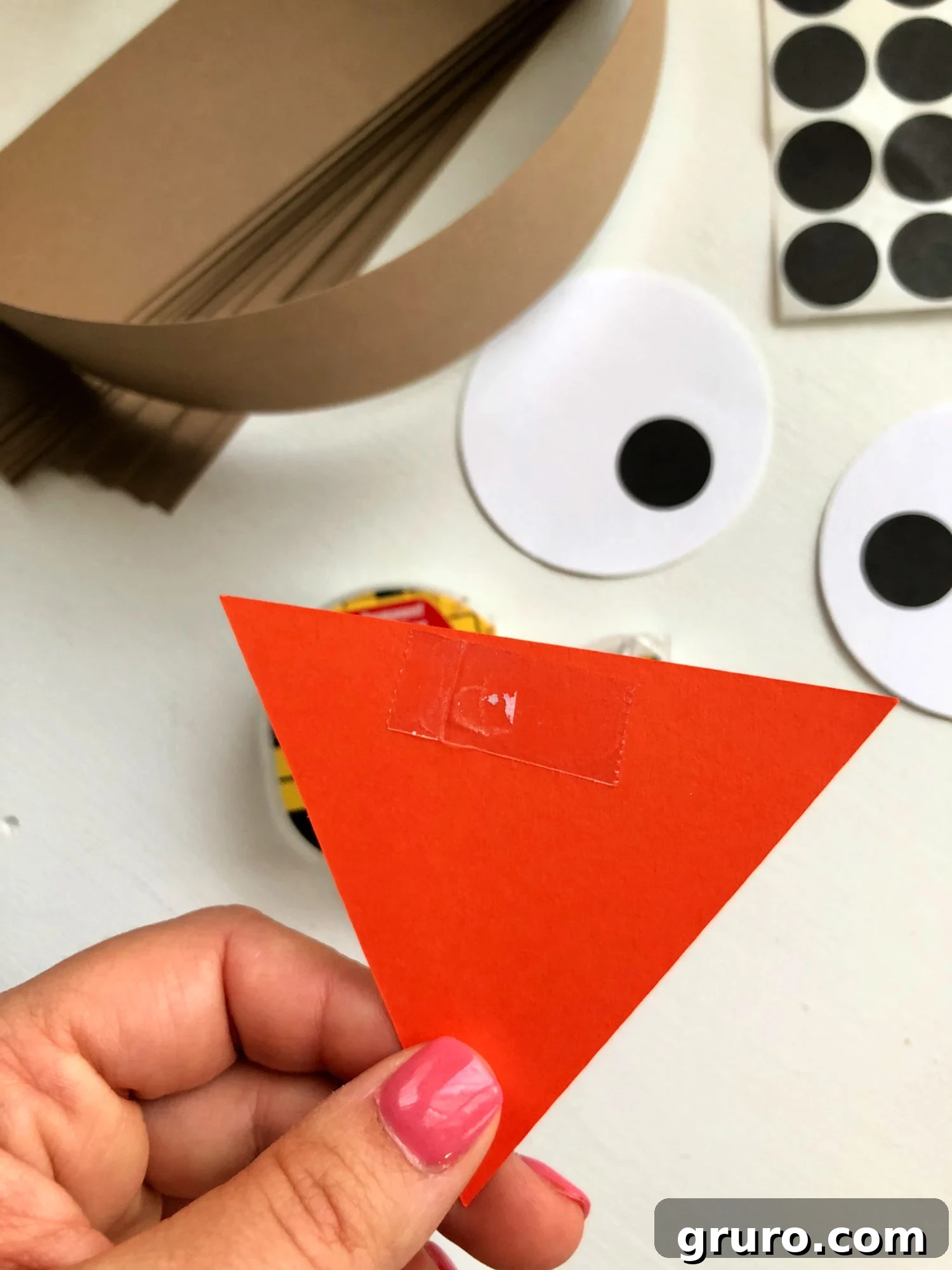 Female hand with pink nails holding an orange paper triangle.