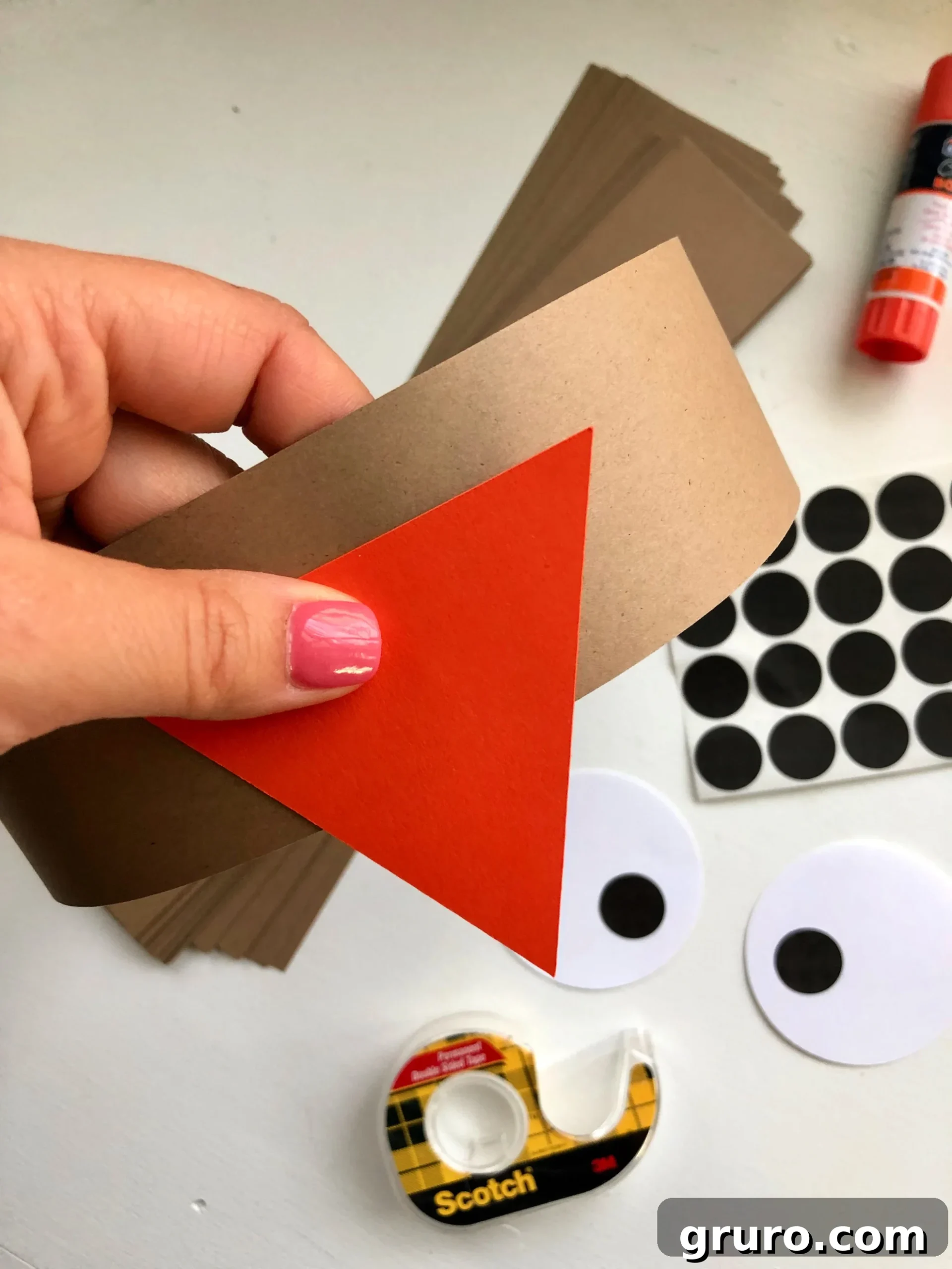 Female hand with pink nails pressing an orange triangle onto a brown circle paper band.