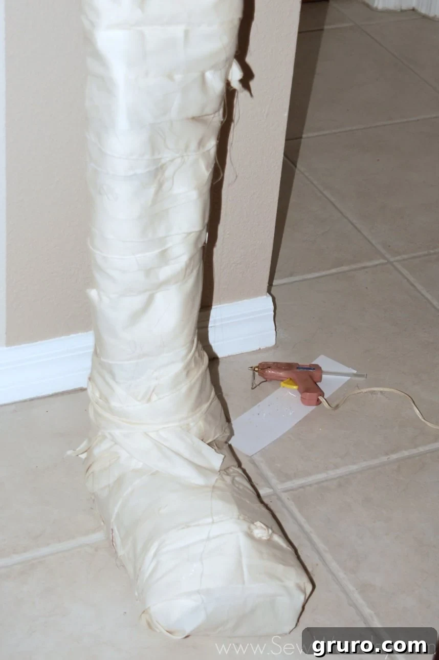 Applying torn and cut muslin strips with hot glue to the mummy's body