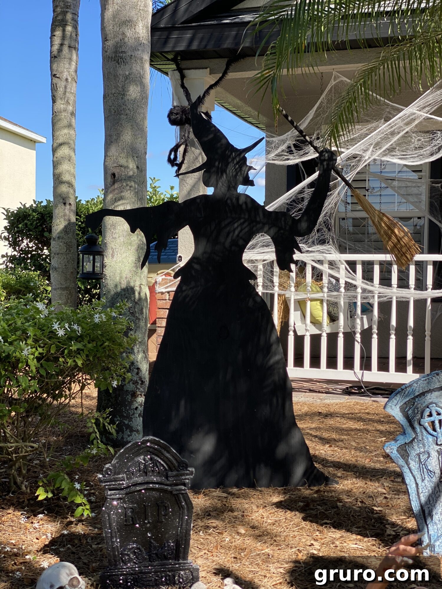 Black witch wood cut out in a yard with cob webs in the background, creating a spooky Halloween atmosphere.