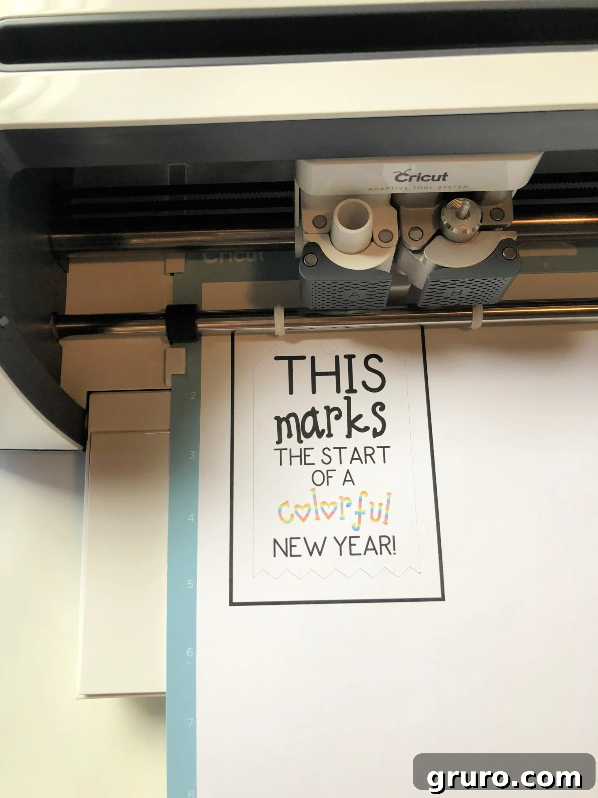 Top view of a Cricut Maker Machine cutting out a paper on a blue mat. 