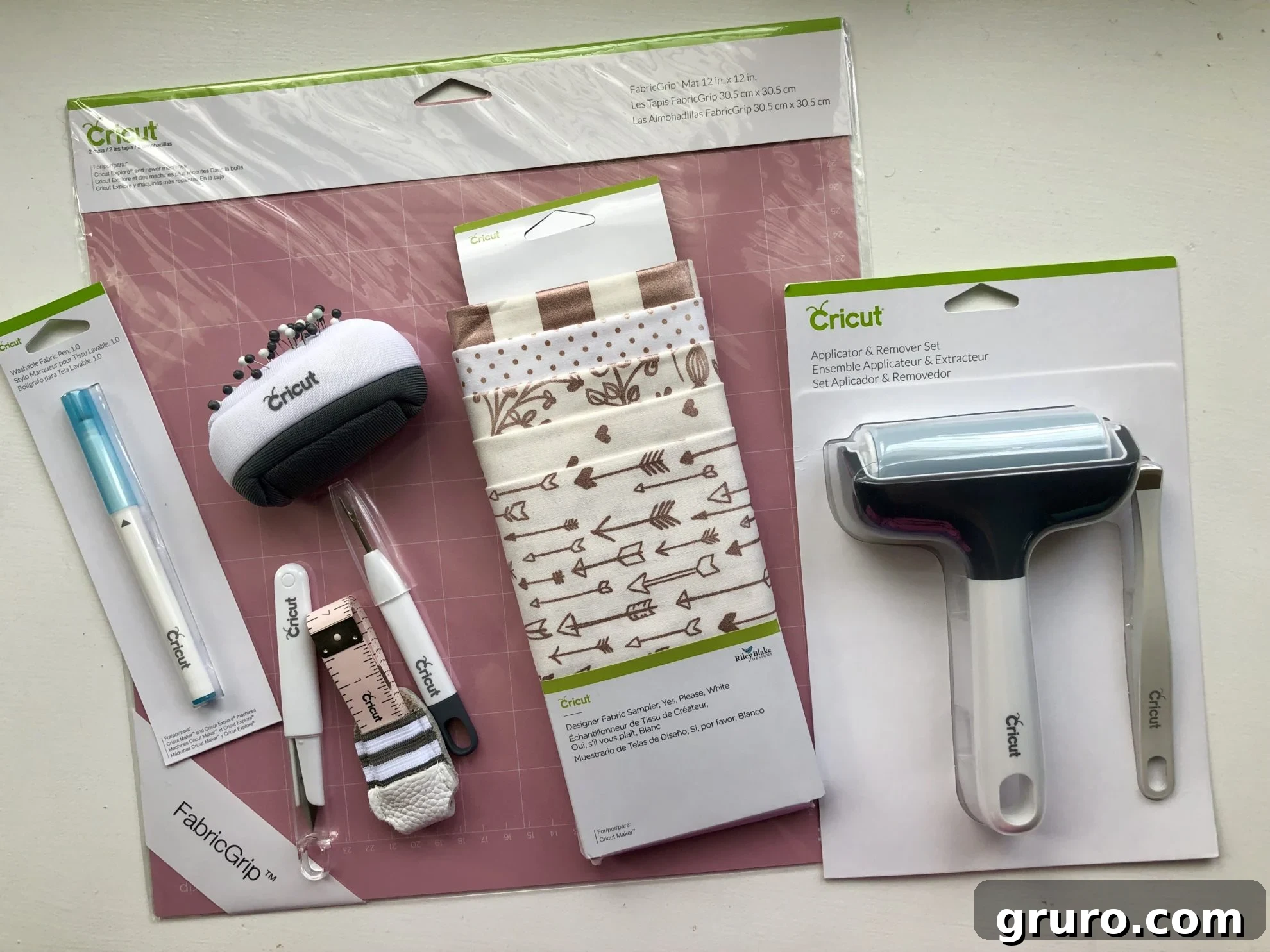 Various Cricut sewing accessories including a FabricGrip Mat, a brayer, fabric swatches, and a pin cushion, arranged for a sewing project.