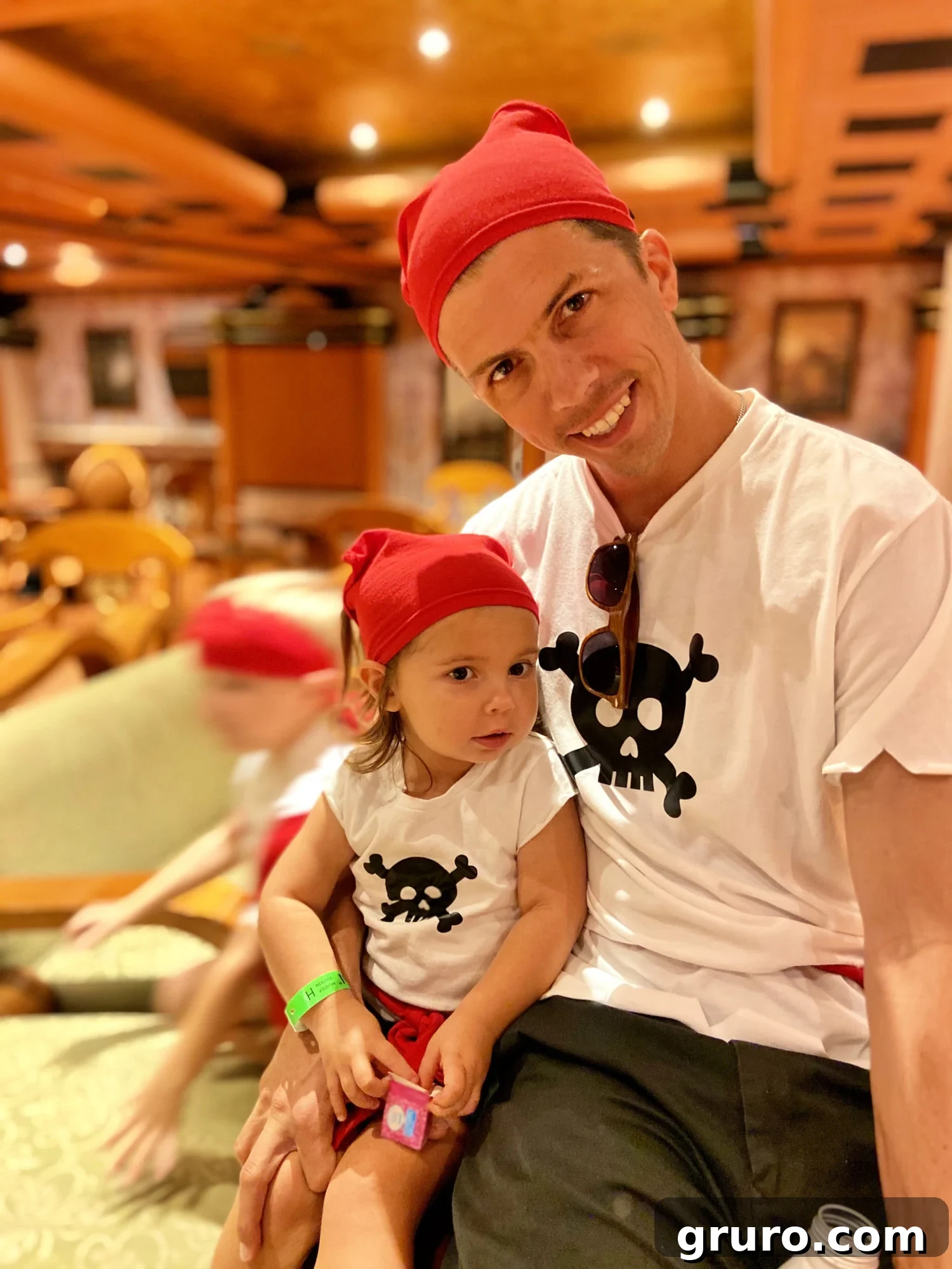 A father and daughter dressed in matching pirate shirts with red du-rags, sharing a tender moment, showcasing the joy of family themed costumes.