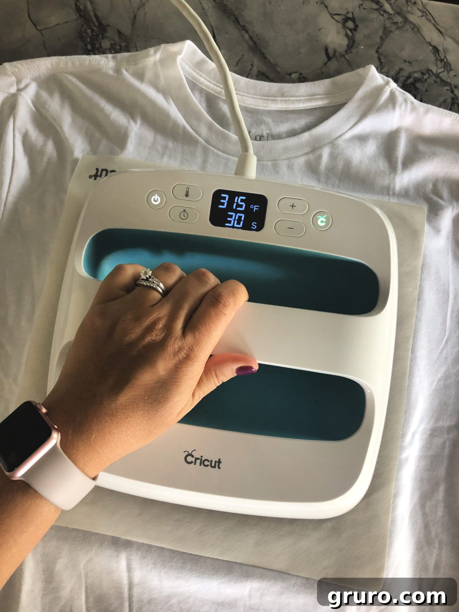 A top-down view of a Cricut EasyPress applying an iron-on design to a white t-shirt, demonstrating the pressing process.