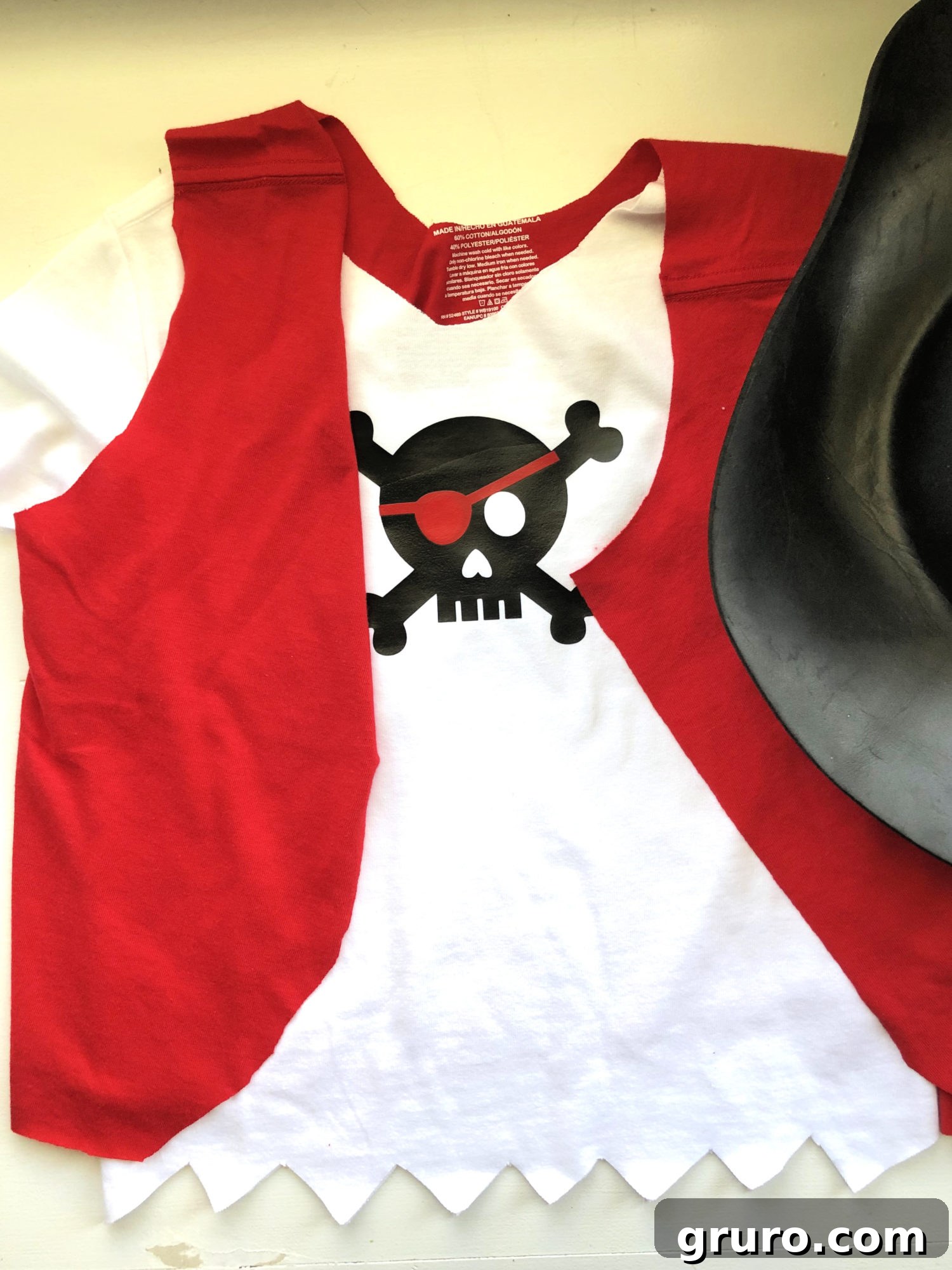 A white pirate shirt with a black skull and crossbones, paired with a cut red cloth vest and a black pirate hat, creating a complete pirate look for a boy.