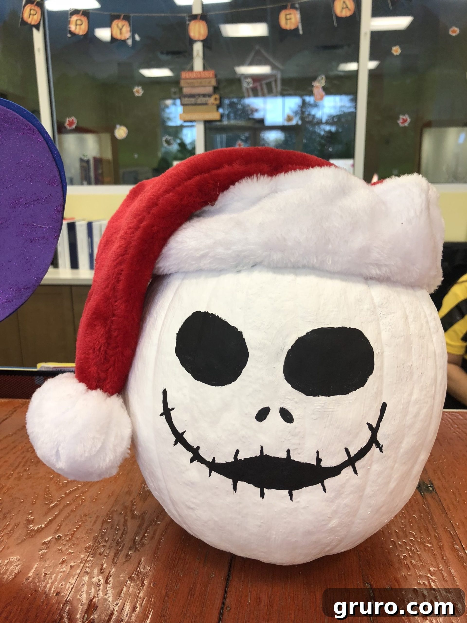 15 Creative No-Carve Pumpkin Decorations 11 A white painted Jack Skellington pumpkin, adorned with a festive red Santa hat.