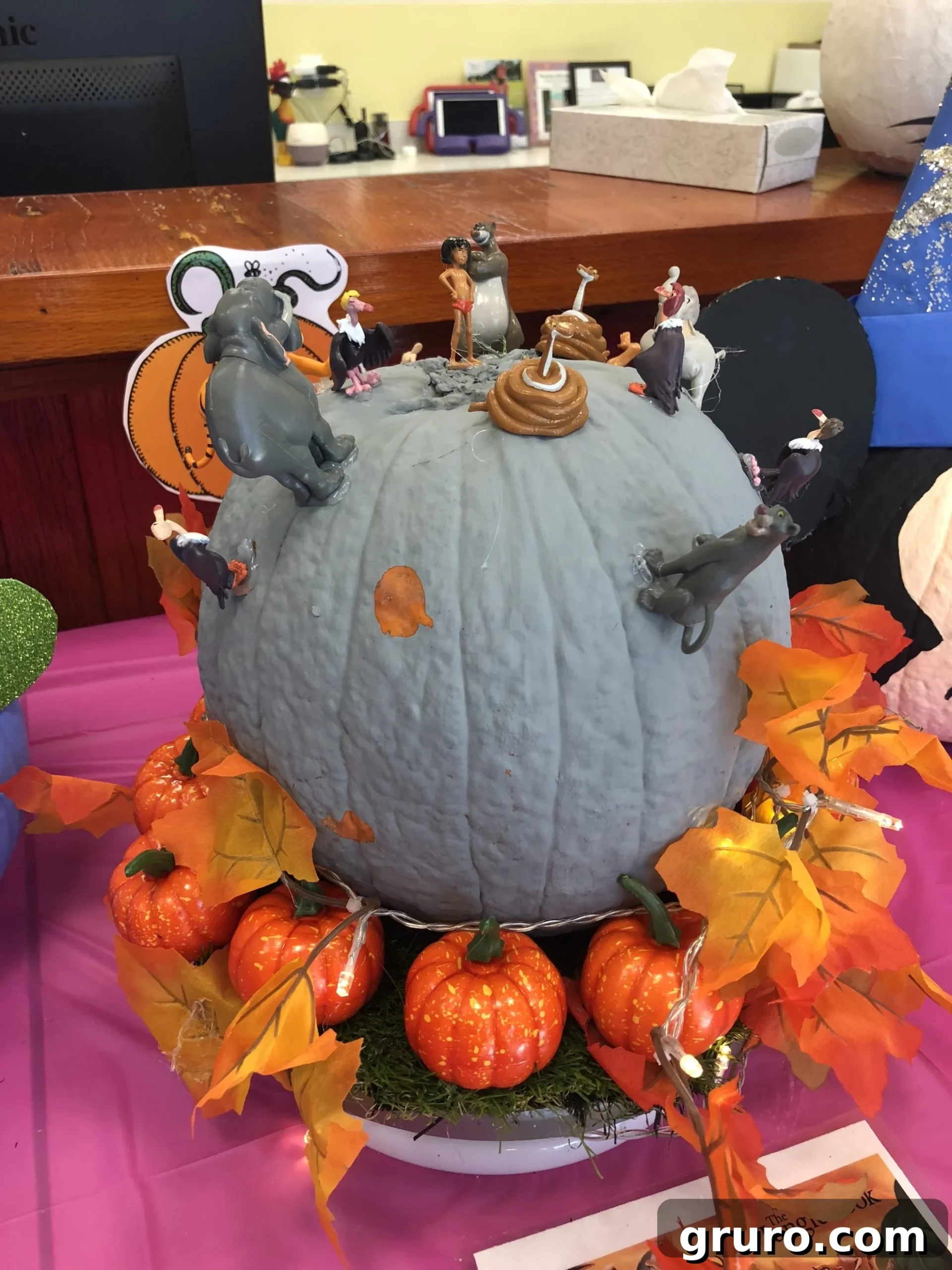 15 Creative No-Carve Pumpkin Decorations 5 A grey painted pumpkin decorated with The Jungle Book character figurines, surrounded by artificial leaves and smaller decorative pumpkins.