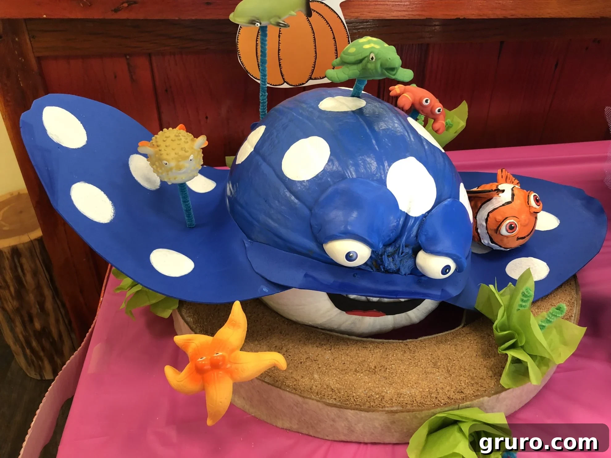 15 Creative No-Carve Pumpkin Decorations 8 Mr. Ray no-carve pumpkin with smaller Nemo and friends figurines arranged around it, on a pink table.