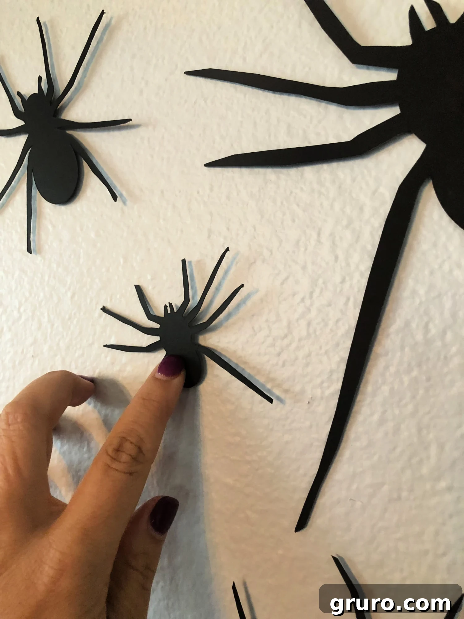 Placing DIY paper spiders on a wall to create a Halloween decoration.