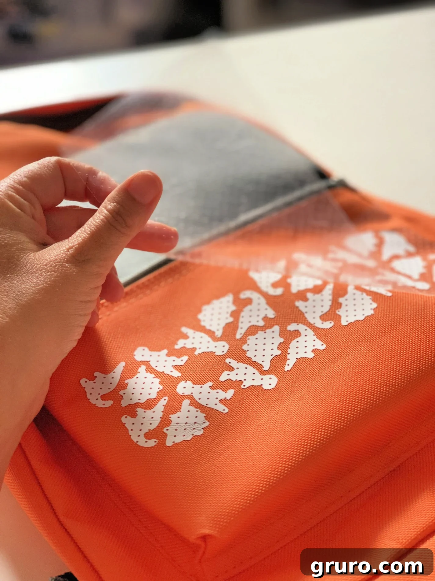 Peeling off mesh iron-on vinyl from a dinosaur backpack