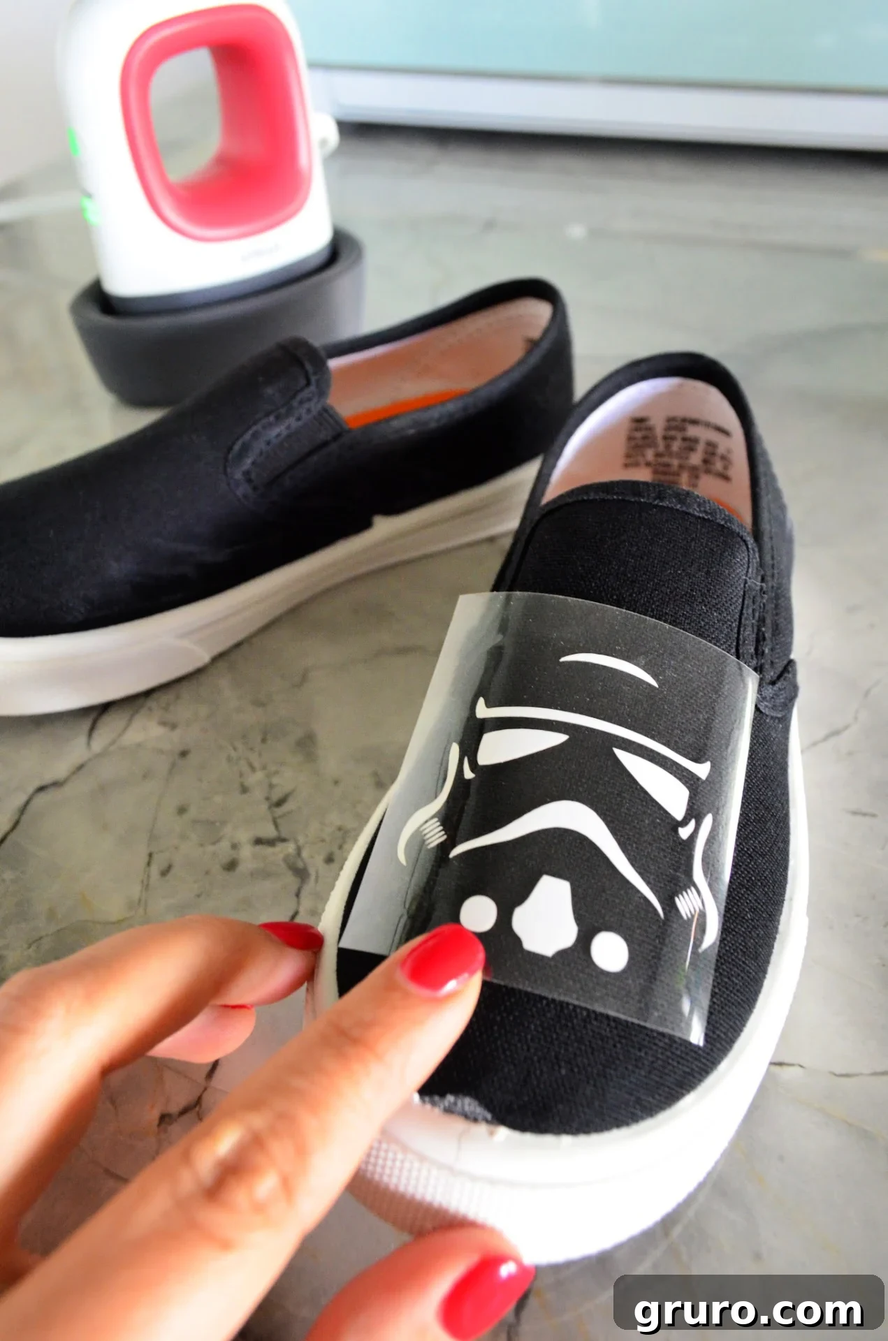 A Stormtrooper helmet iron-on vinyl design being carefully positioned on the front of a white canvas shoe before heat application with a Cricut EasyPress Mini.