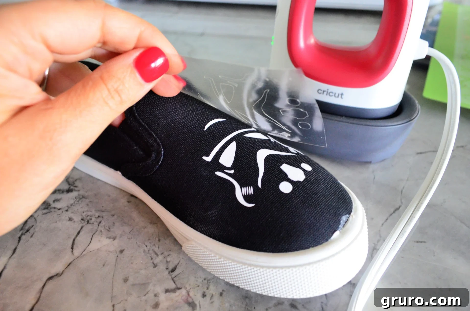 A hand gently peeling off the clear transfer tape from a perfectly adhered Stormtrooper helmet design on a canvas shoe after applying heat with the EasyPress Mini.
