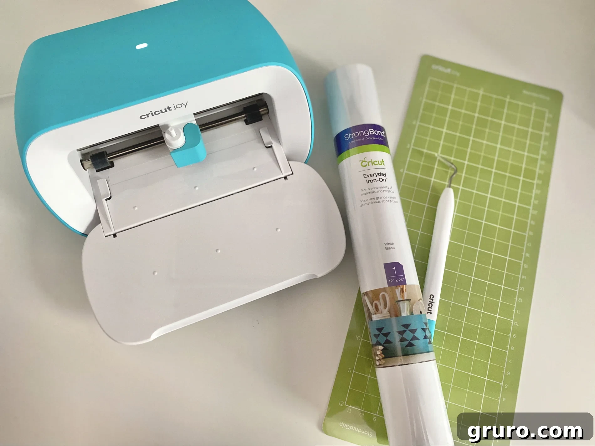 A collection of essential supplies for creating iron-on vinyl labels for soft bins: Cricut Joy machine, Iron-On Vinyl in a chosen color, a weeding tool for precision, and a Green StandardGrip Mat.