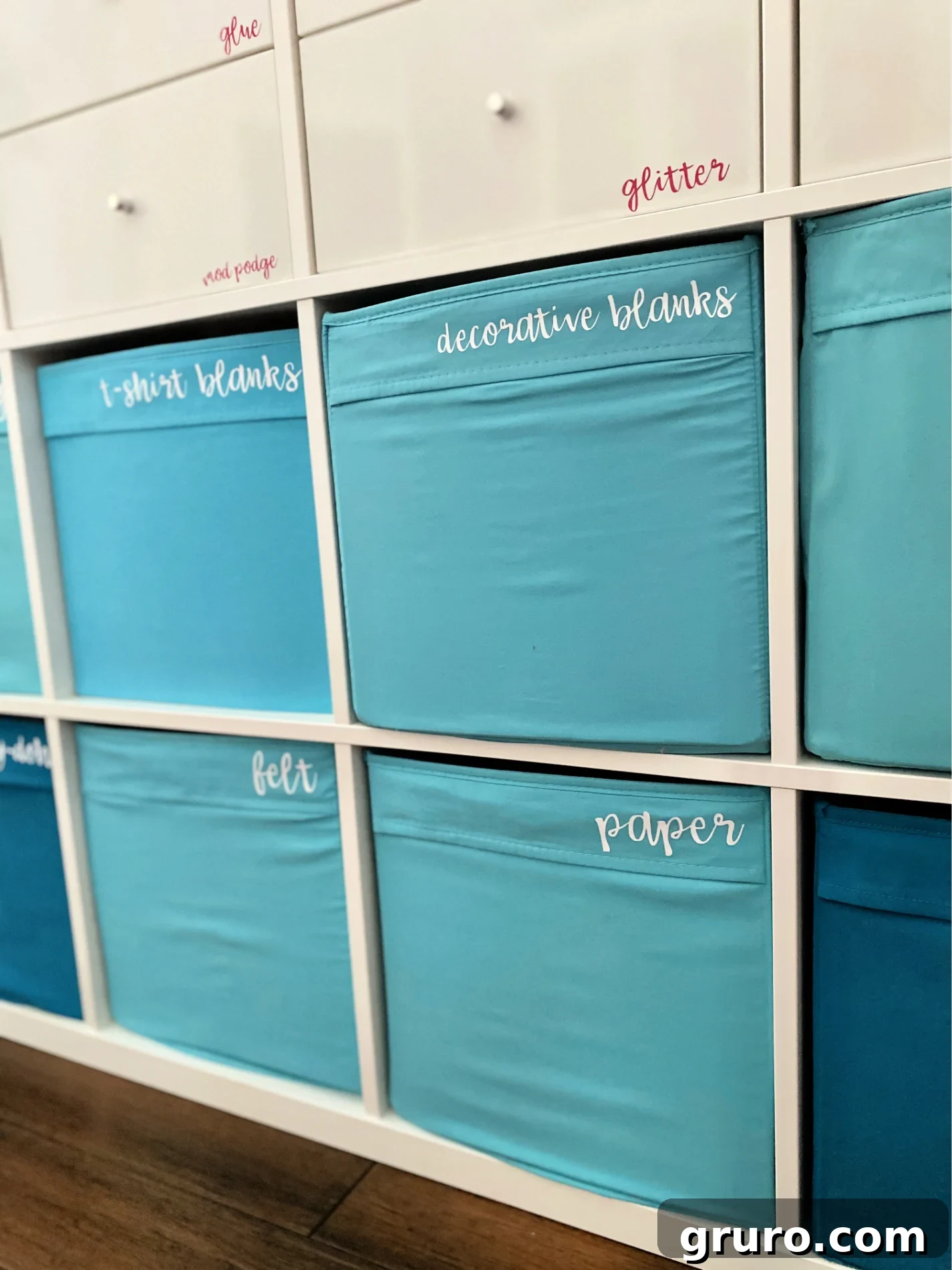 A pristine white cube shelf unit neatly filled with blue cloth bins, each prominently featuring white iron-on vinyl text labels. This image beautifully illustrates an organized and accessible storage solution.