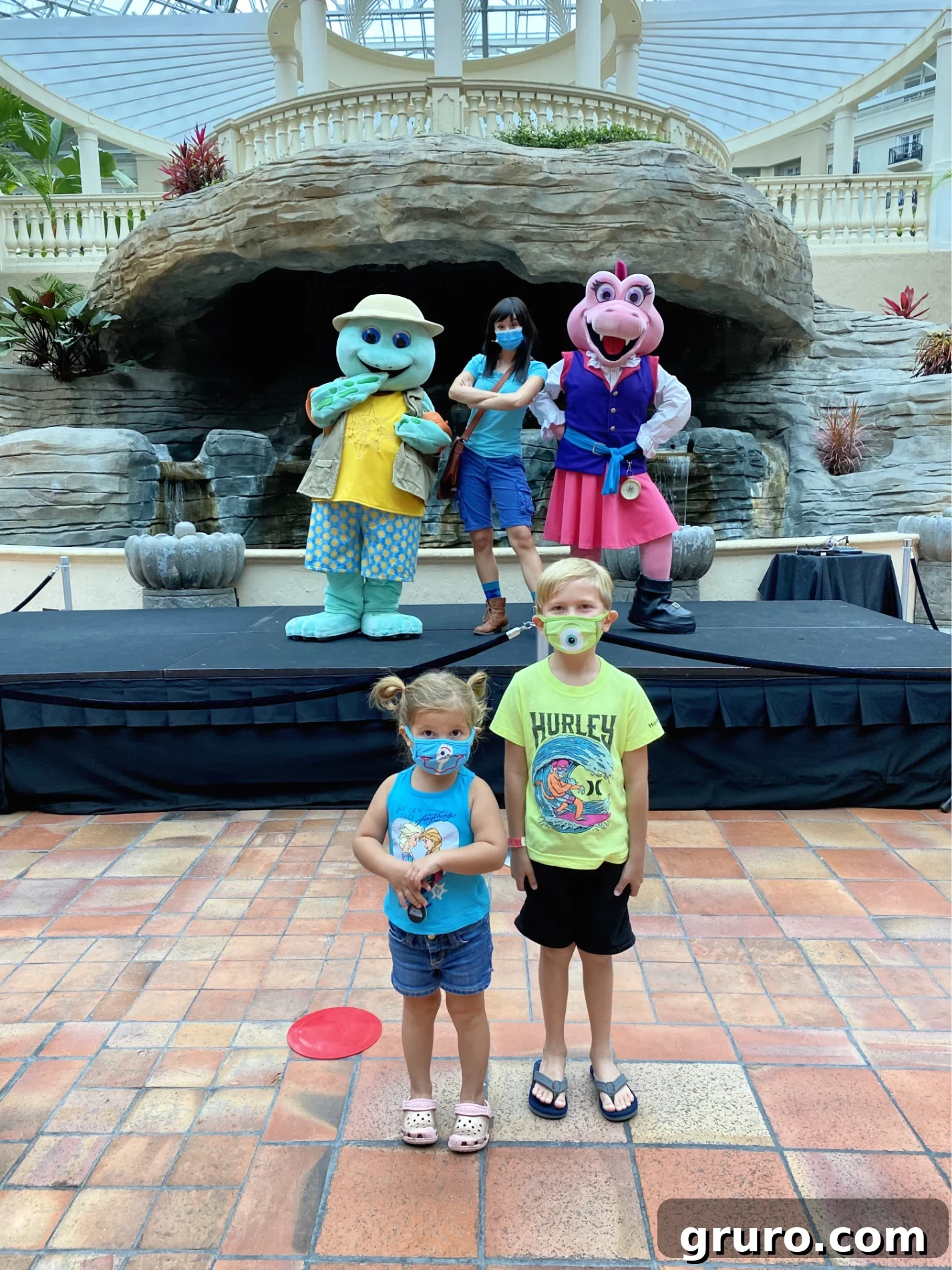 Boy and girl standing with mask with characters on stage behind them.