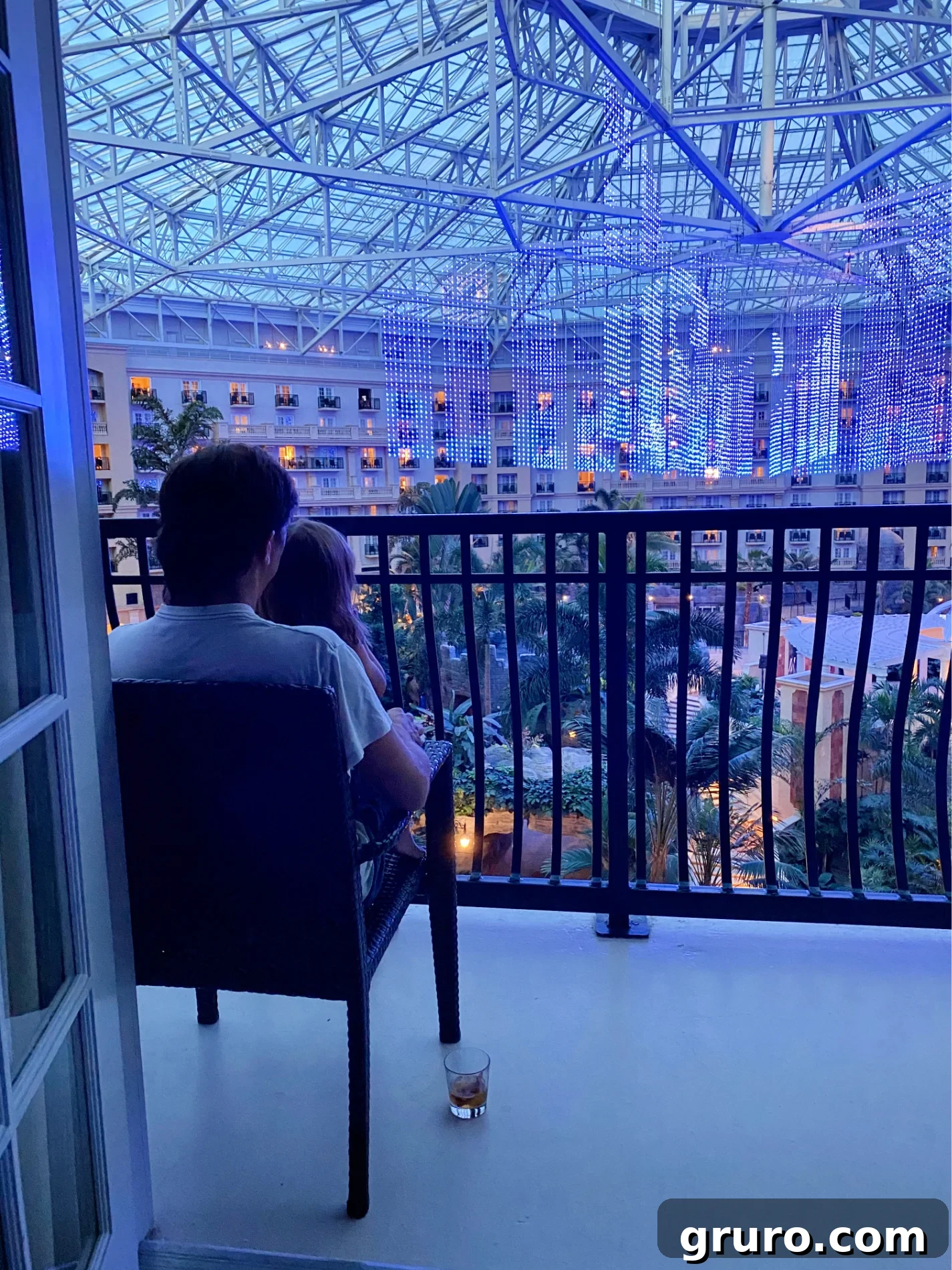 Child sitting on father's lap on balcony watching light show in hotel.