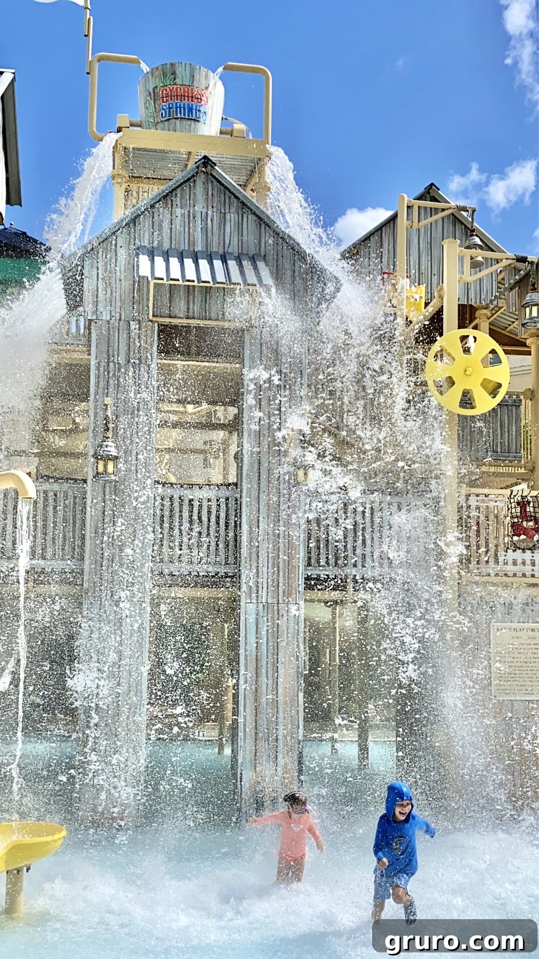 Two children running in a water park after water dumping on them. 