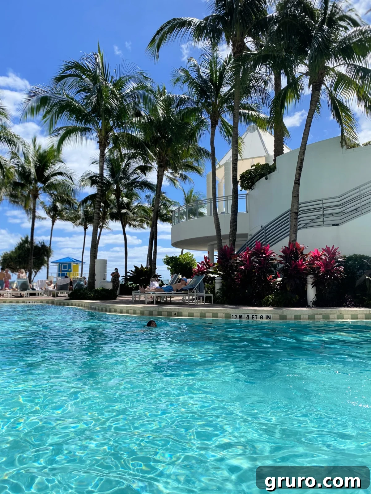A bright blue swimming pool with a child happily swimming in the clear water at The Diplomat Beach Resort.