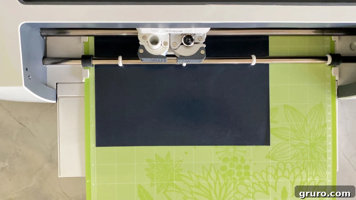 White Cricut machine with green mat and black iron-on vinyl on mat.