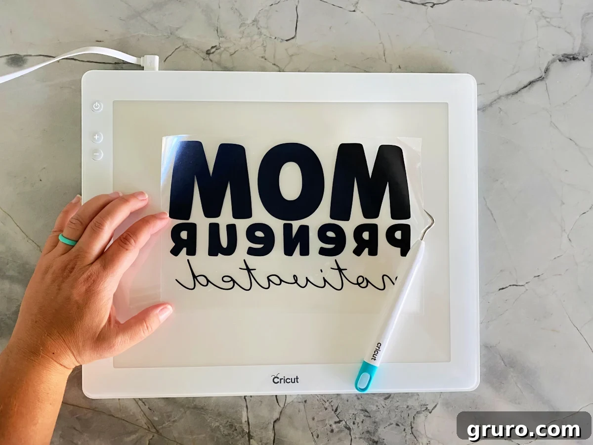 Cricut BrightPad with weeded iron-on vinyl and weeding tool.