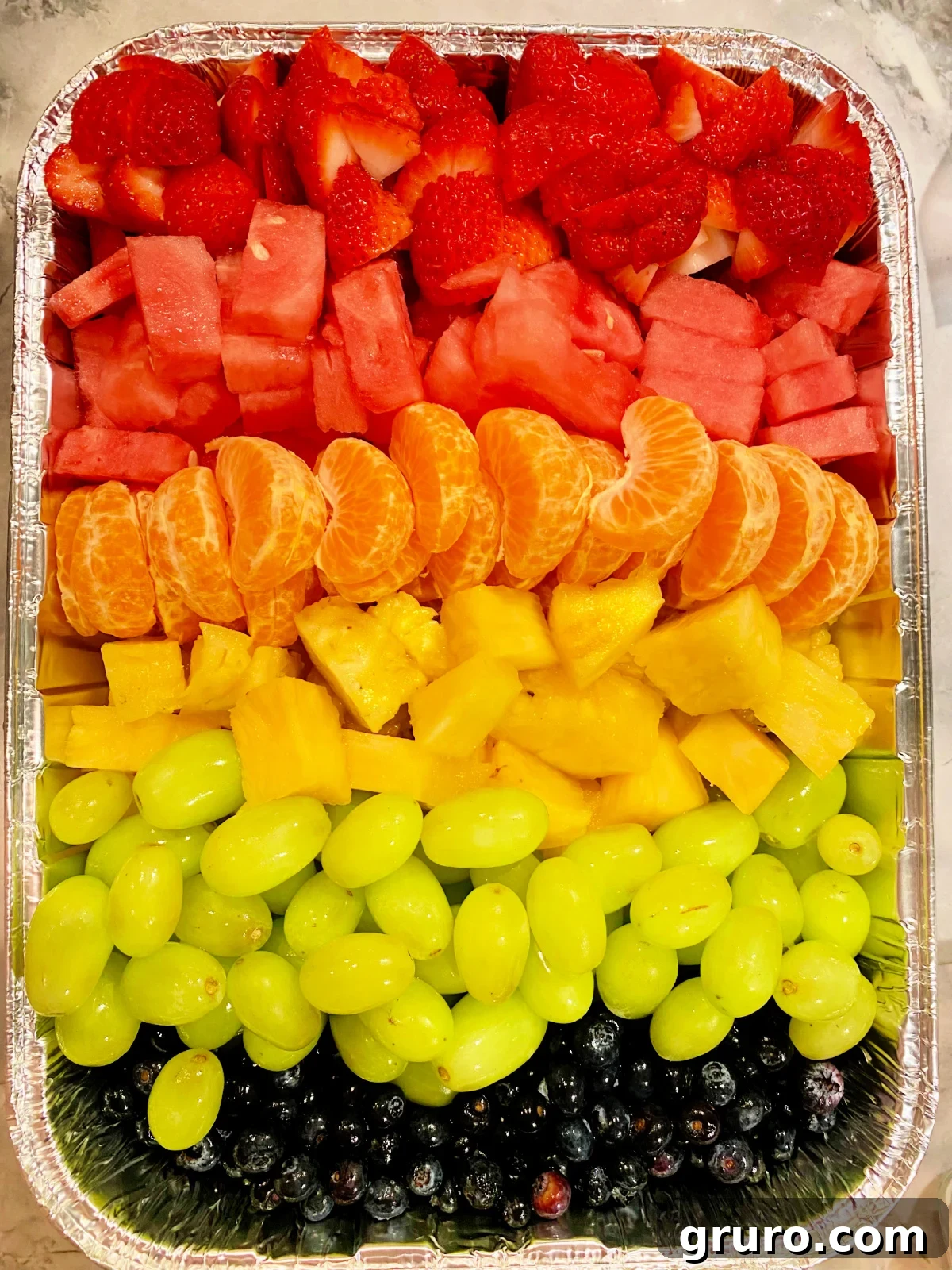 Rainbow fruit tray with strawberry, watermellon, oranges, pineapple, green grapes, and bueberries.