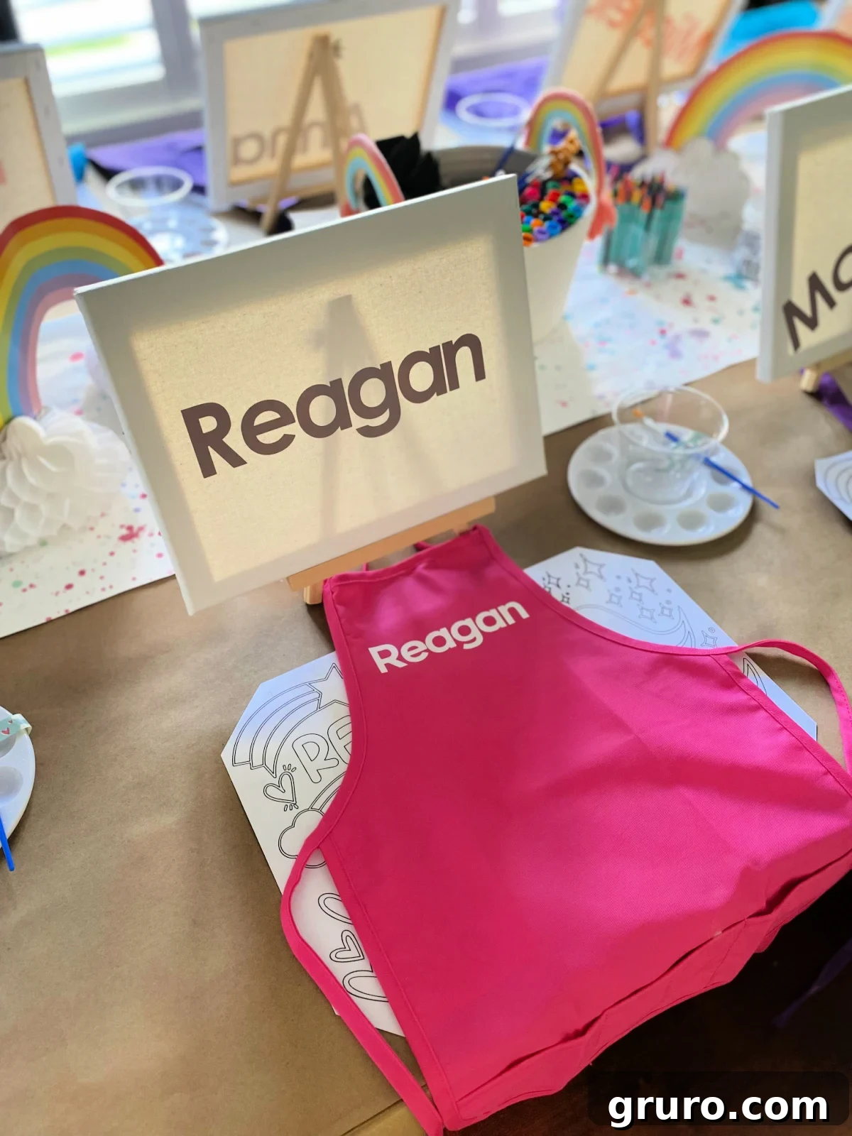 Canvas with name on it and pink apron ontop of table.