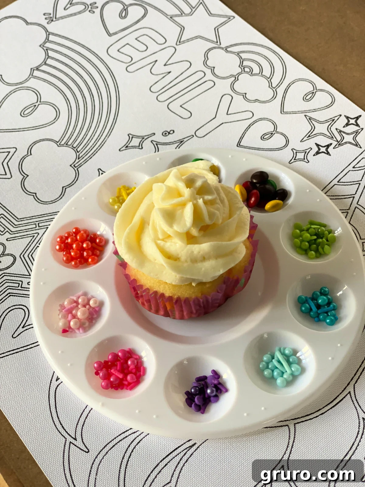Close up of a paint palette filled with sprinkles with a vanilla frosted cupcake.